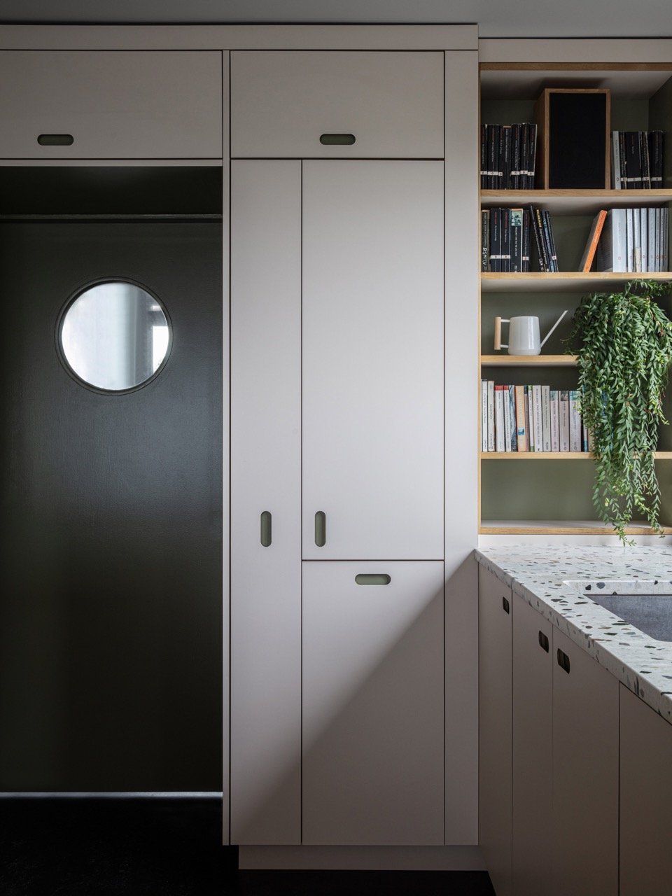 Close-up of white kitchen cabinetry and a bookshelf with books and a potted plant.