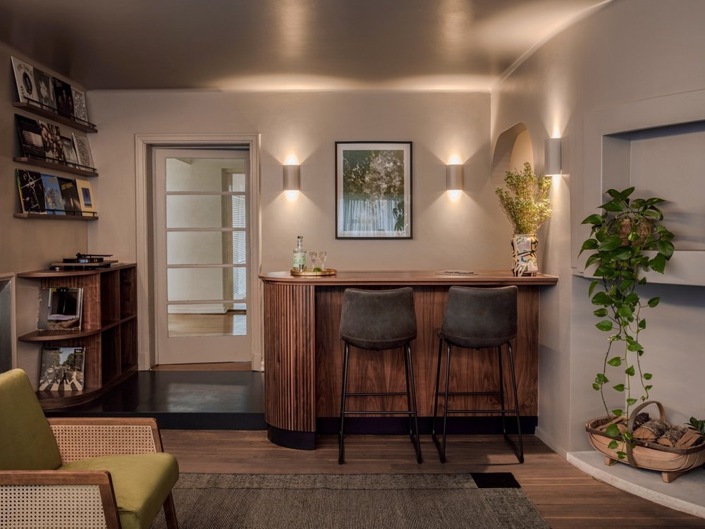 Living room with a wooden bar, two chairs, a houseplant, and wall-mounted lights.