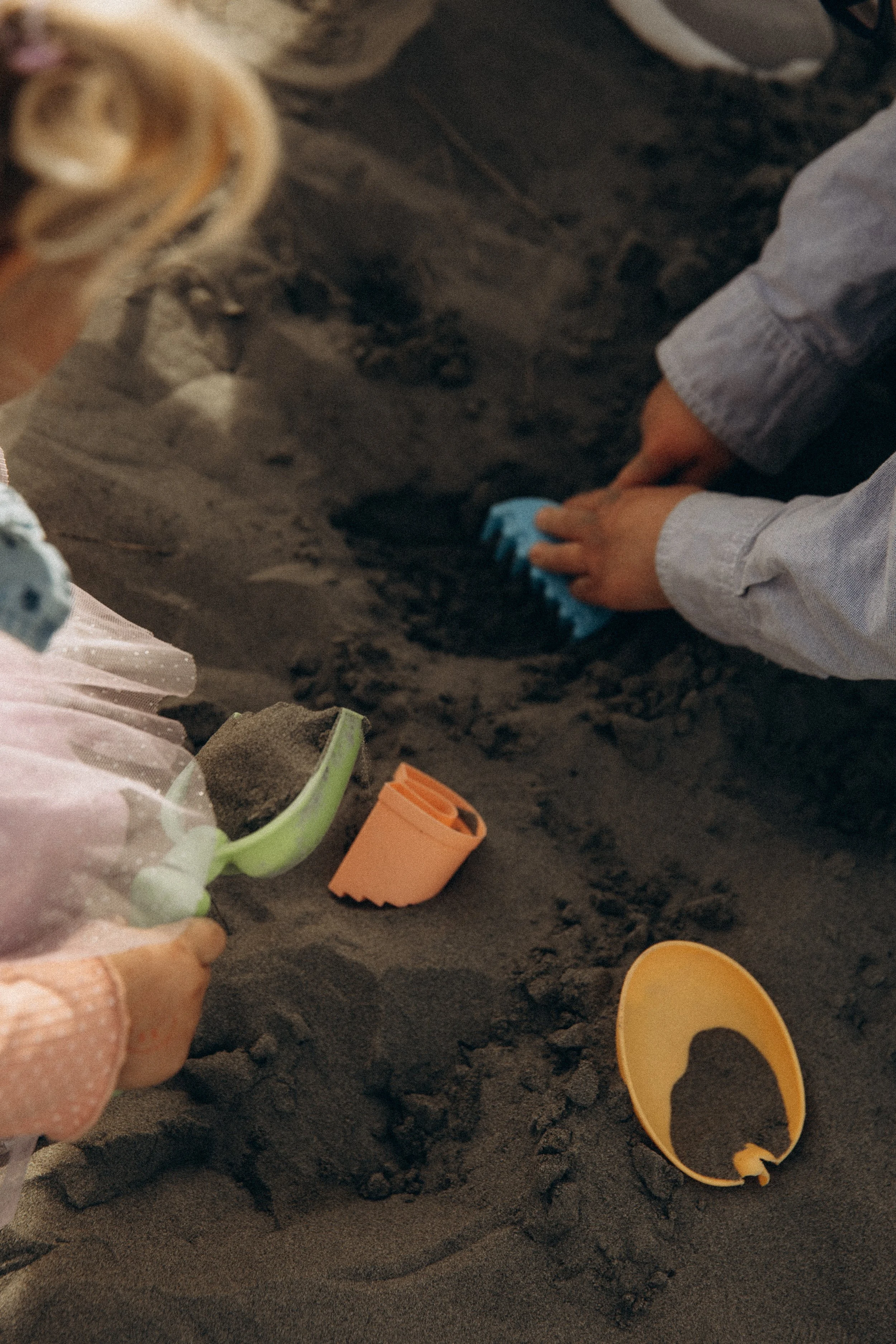 Children playing in the sand with toy shovels and sand molds.