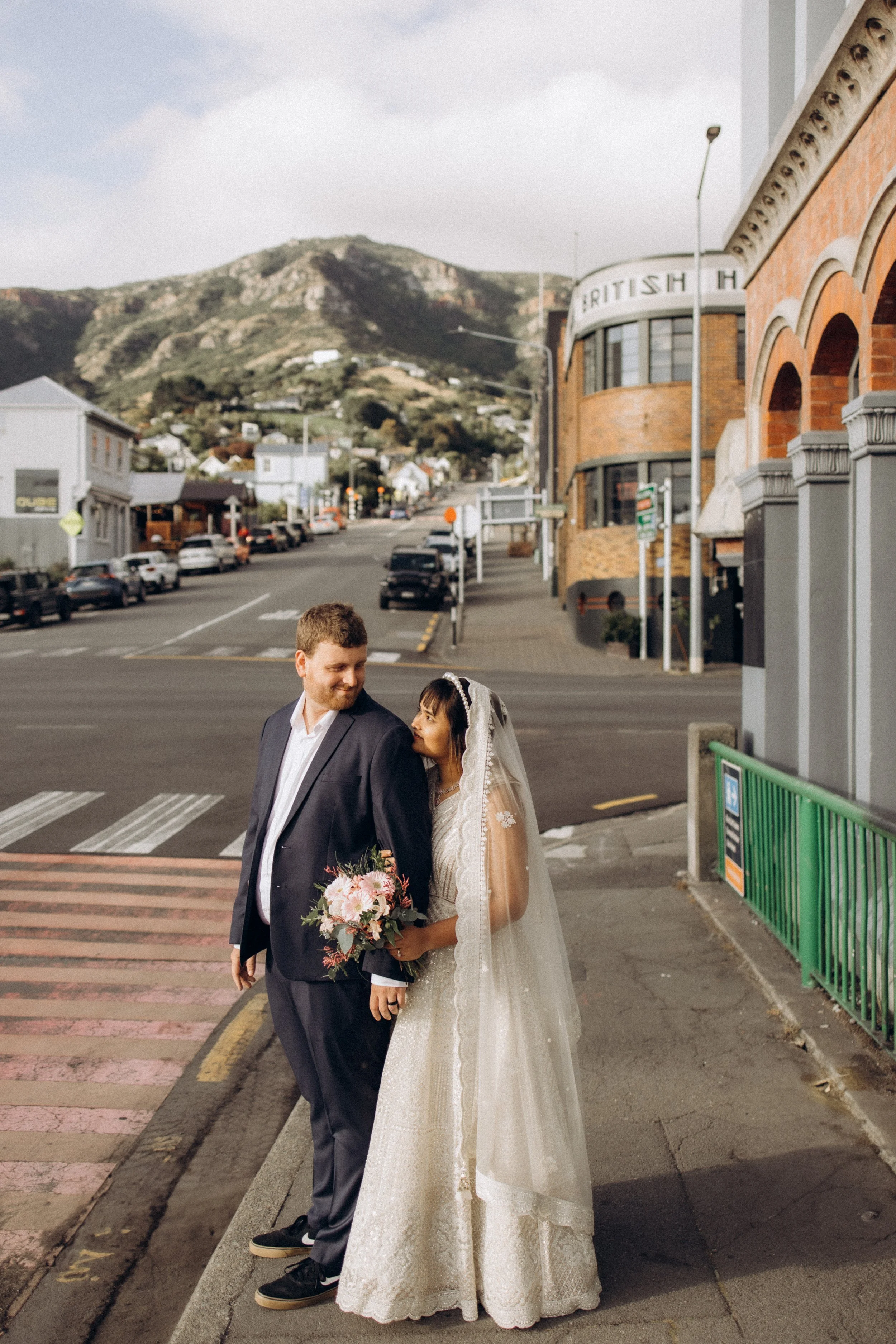Bride and groom standing on a street corner with mountains in the background.