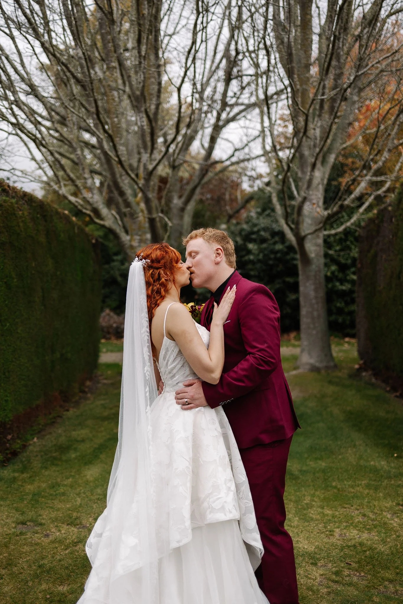 Newlyweds kissing beneath autumn trees in the gardens at Trott’s Garden