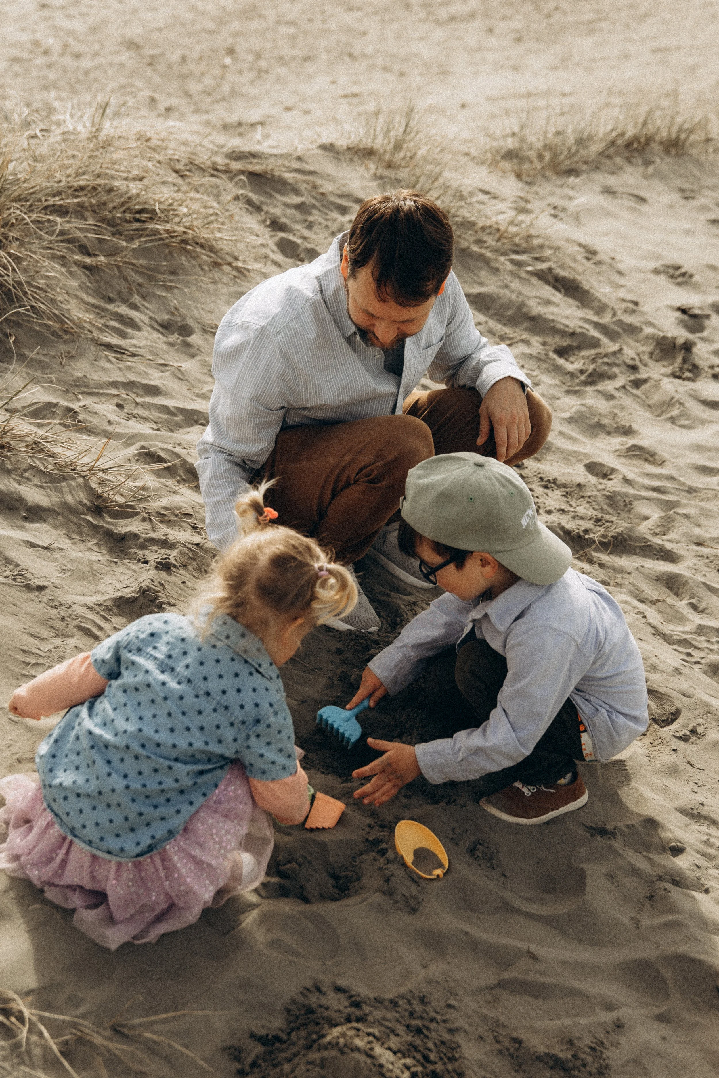 A man and two children playing in the sand with toys.