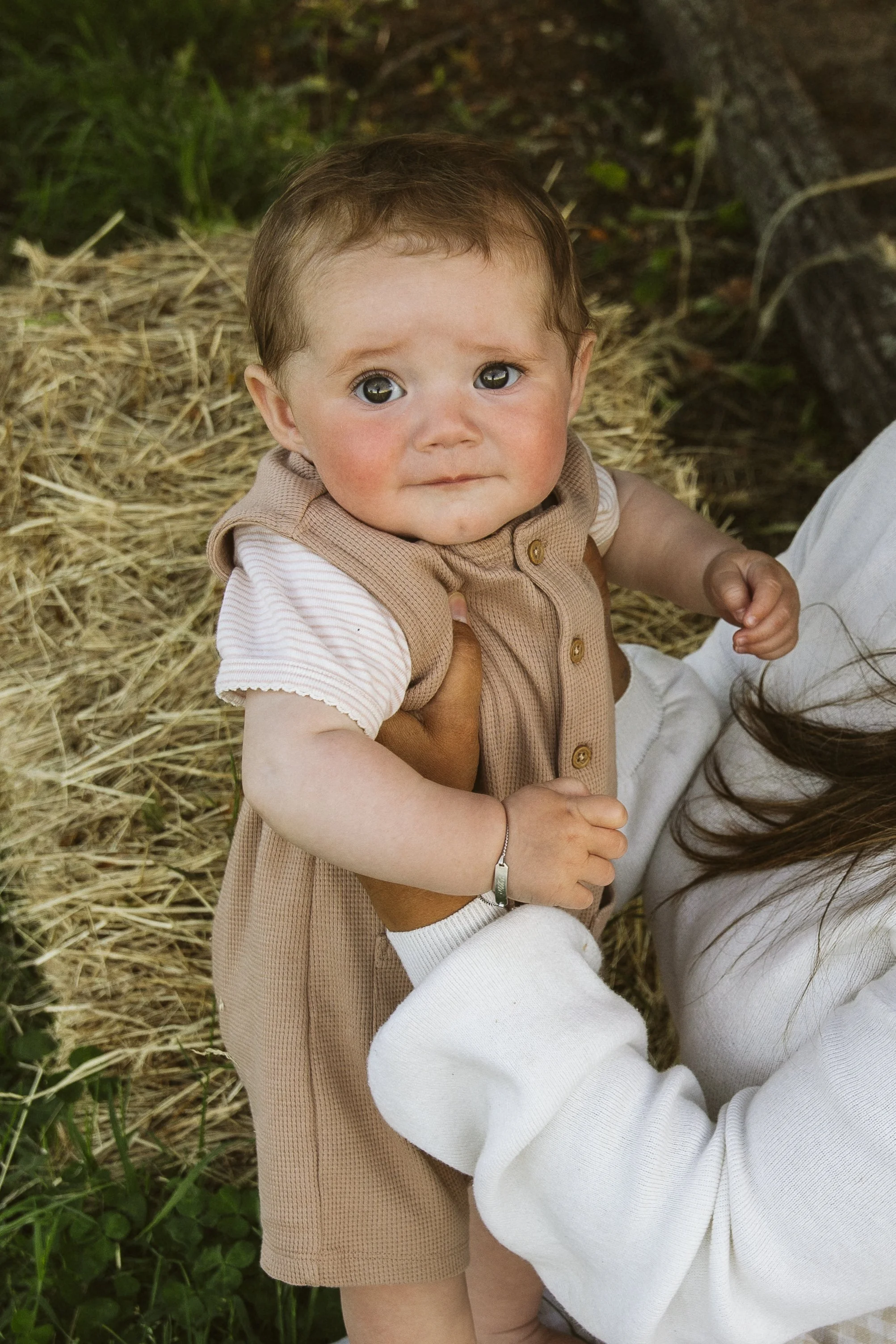 Baby being held by a person with hay in the background.