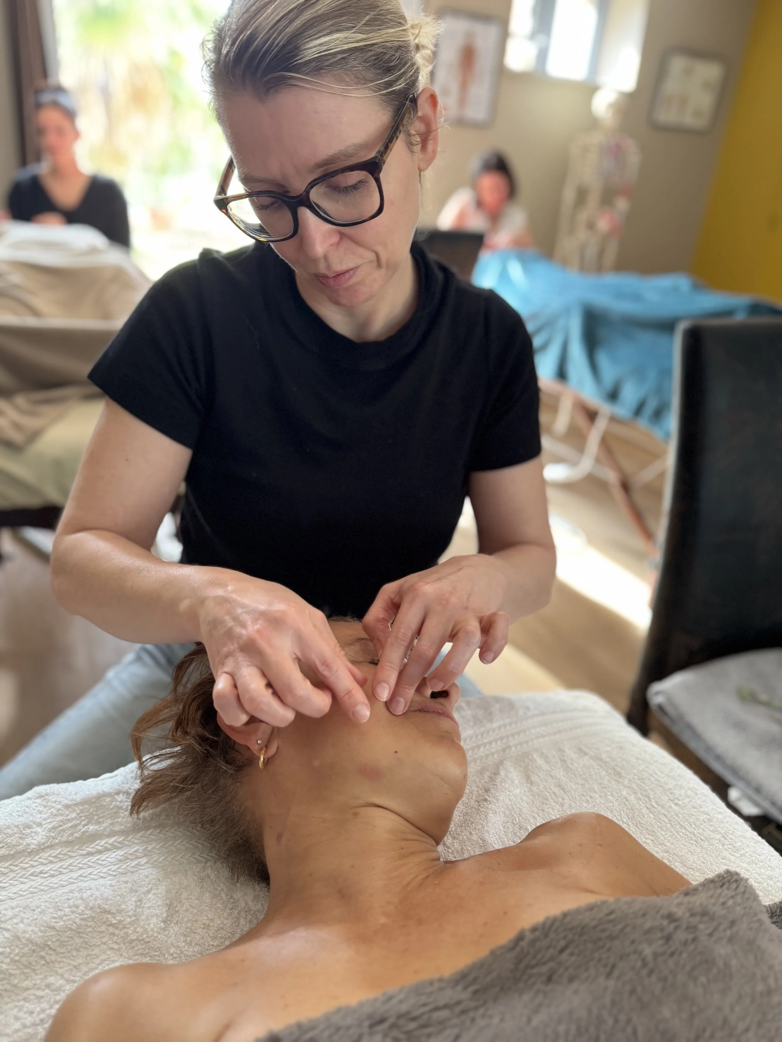Une esthéticienne effectue un massage facial s'appelant kobido visage sur une femme allongée sur une table de massage.
