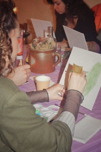Personnes peignant sur des toiles autour d'une table, avec des fournitures artistiques et un vase au centre.