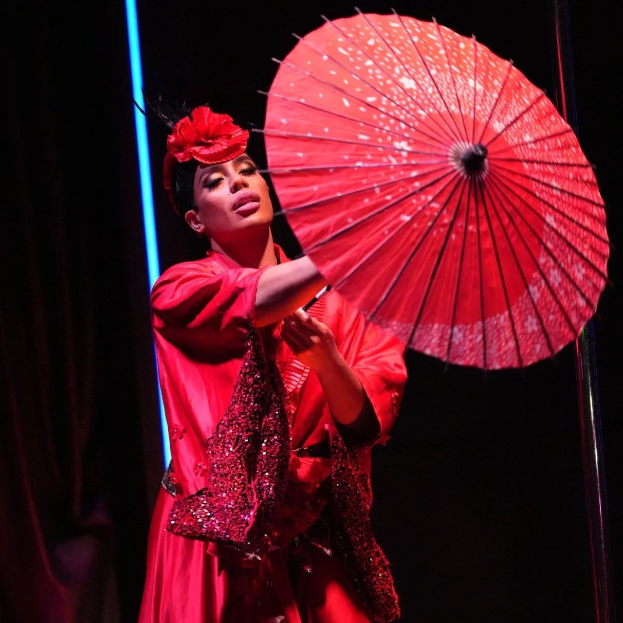Performer dressed in red holding a red paper parasol on stage.