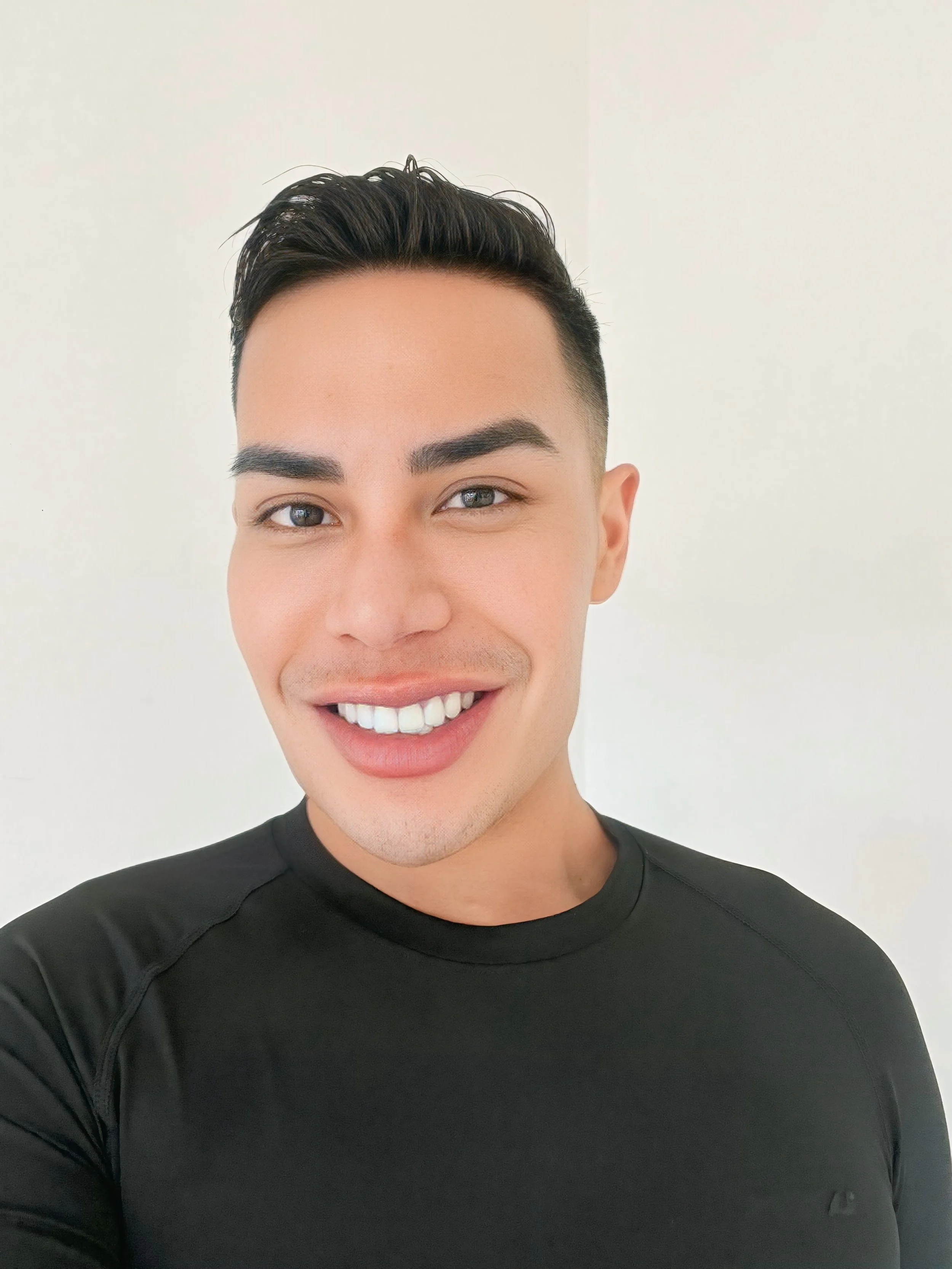 A smiling young man with dark hair, light skin, and blue eyes wearing a black shirt standing against a plain white background.
