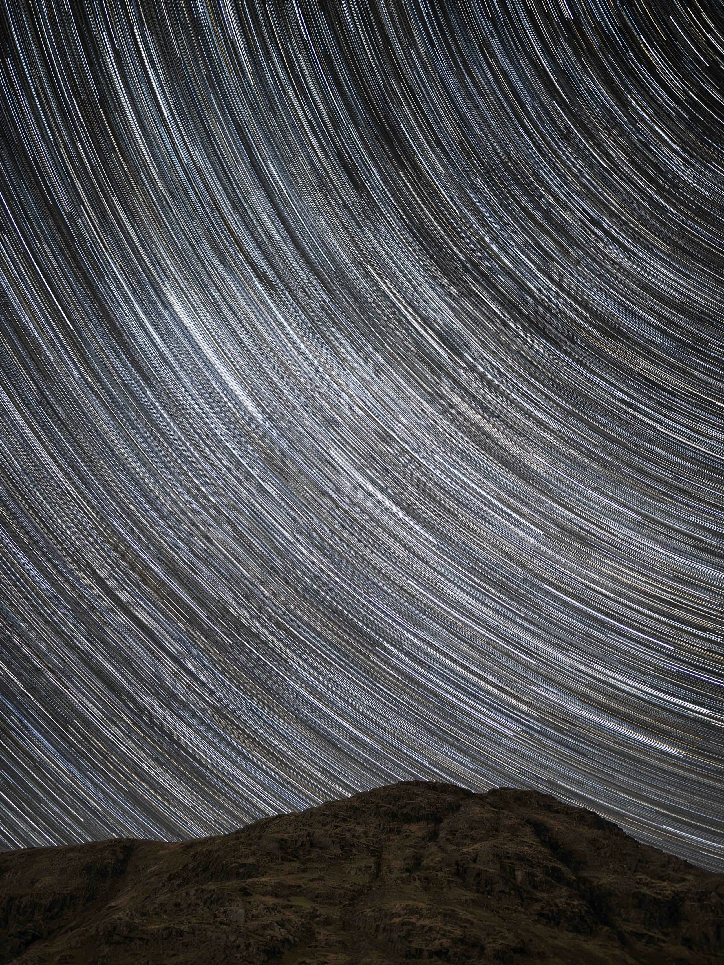 Star trails in the night sky above a mountain landscape.