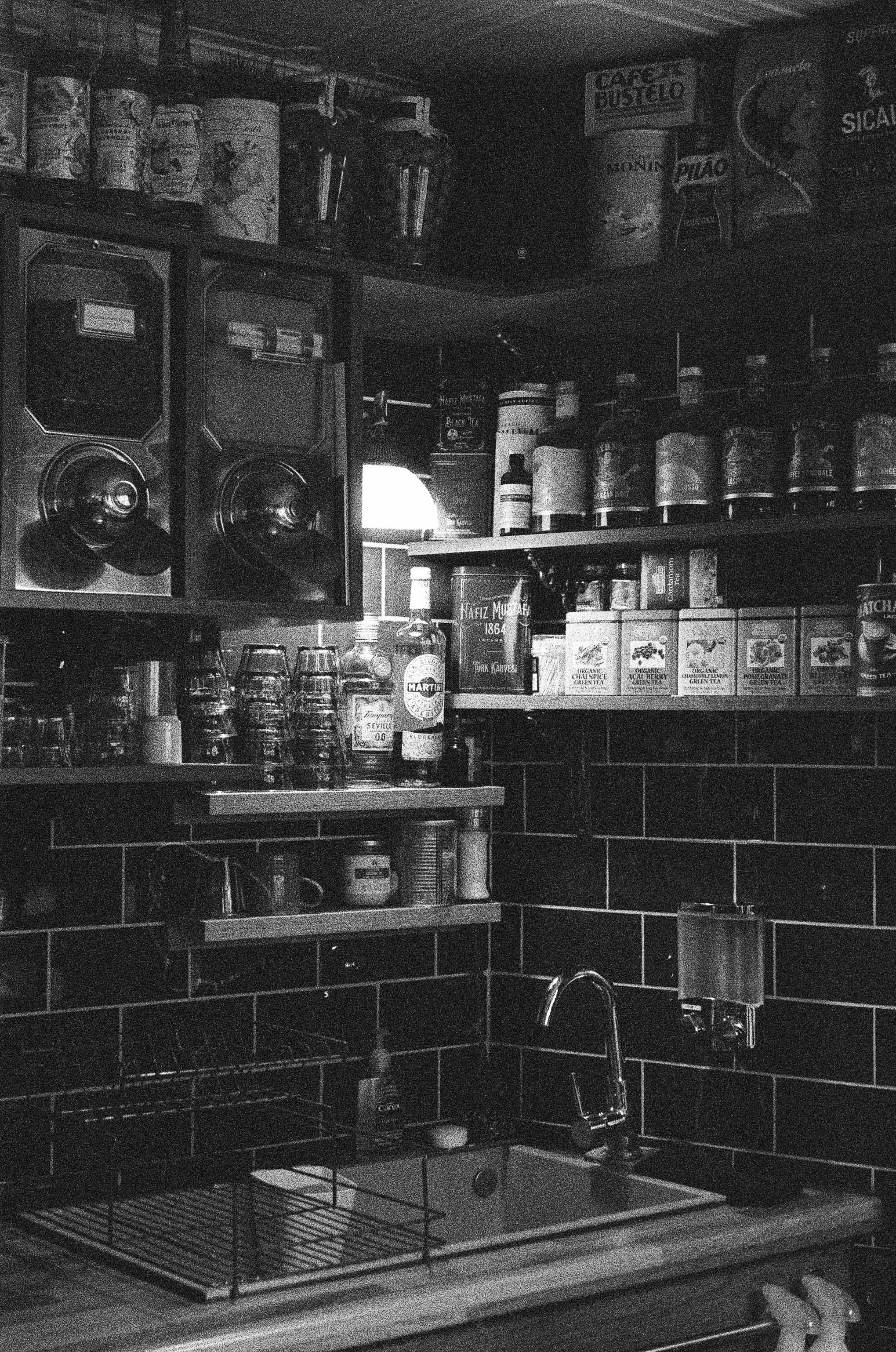 a small lamp light up bottles on a shelf in a small coffee shop, photo on delta 3200