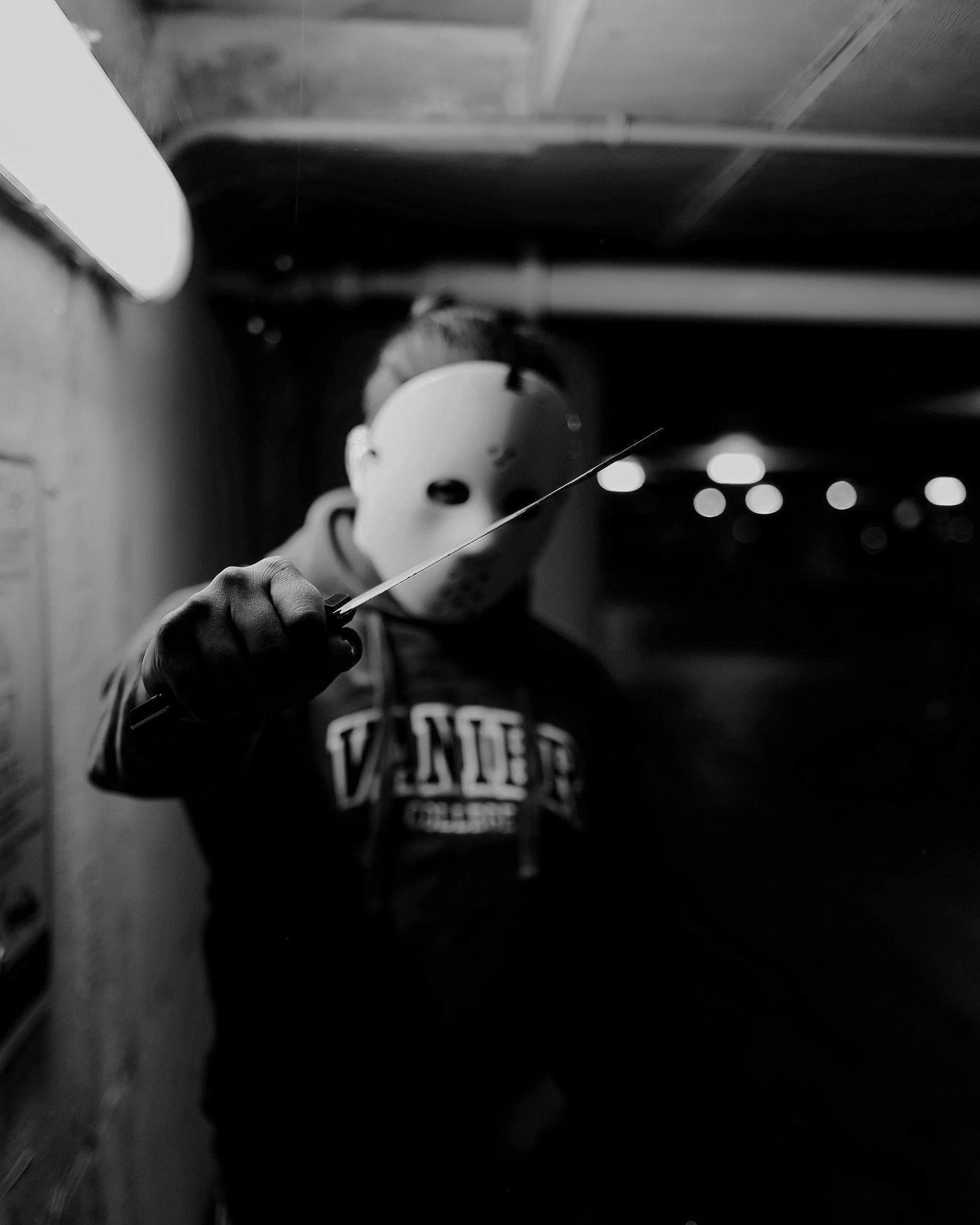 Person wearing a hockey mask and gloves holding a sharp object in dark lighting.