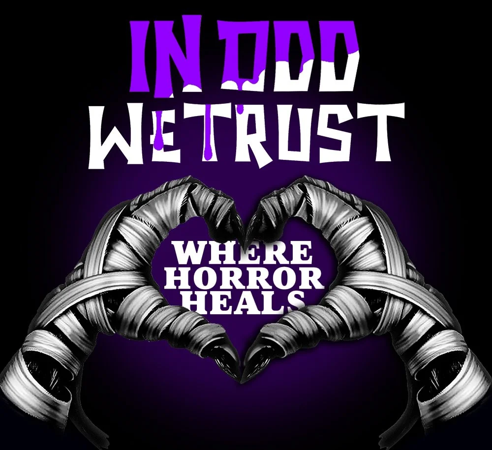 A Halloween-themed display with a black background, featuring silver, mummy-like hands forming a heart shape around the words 'WHERE HORROR HEALS' in white text. Above, the phrase 'IN ODDD WE TRUST' is written in mismatched purple and white letters.