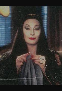 Anjelica Huston as Morticia Addams knitting