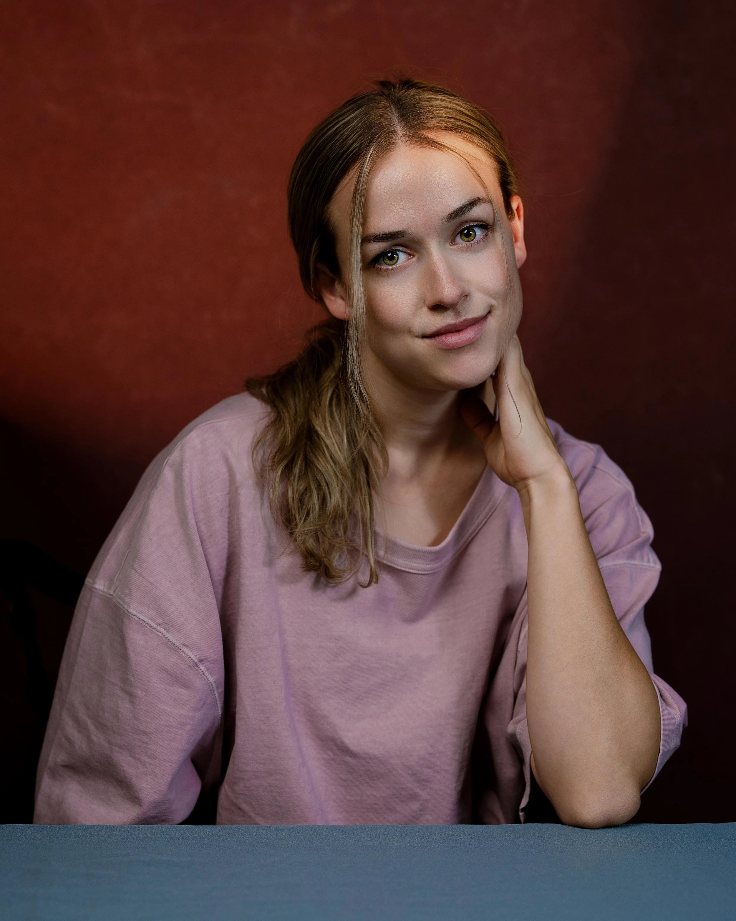 Portrait headshot of female actor in pink with red backdrop and blue table