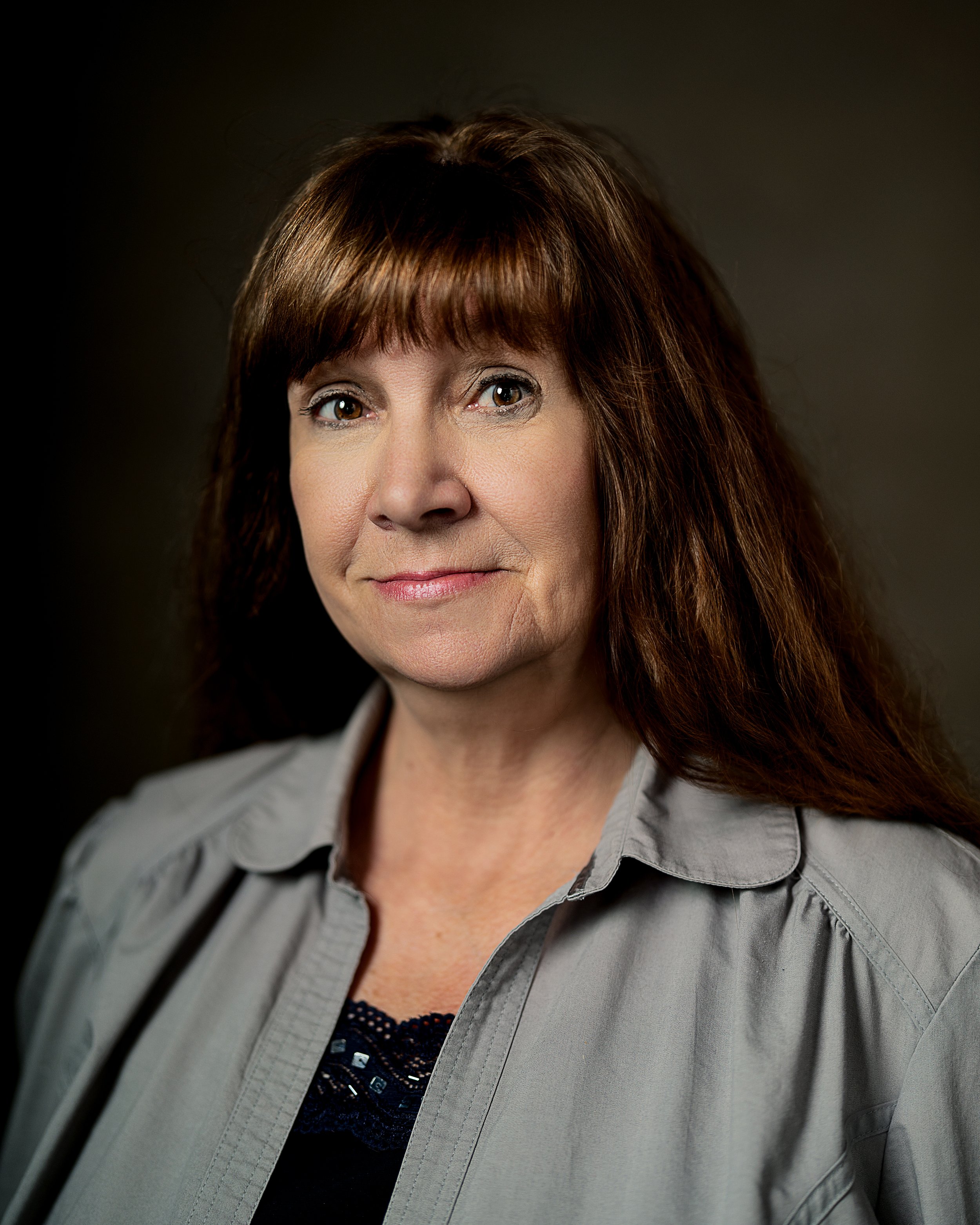 Headshot of woman with brown hair in fronto of olive green backdrop