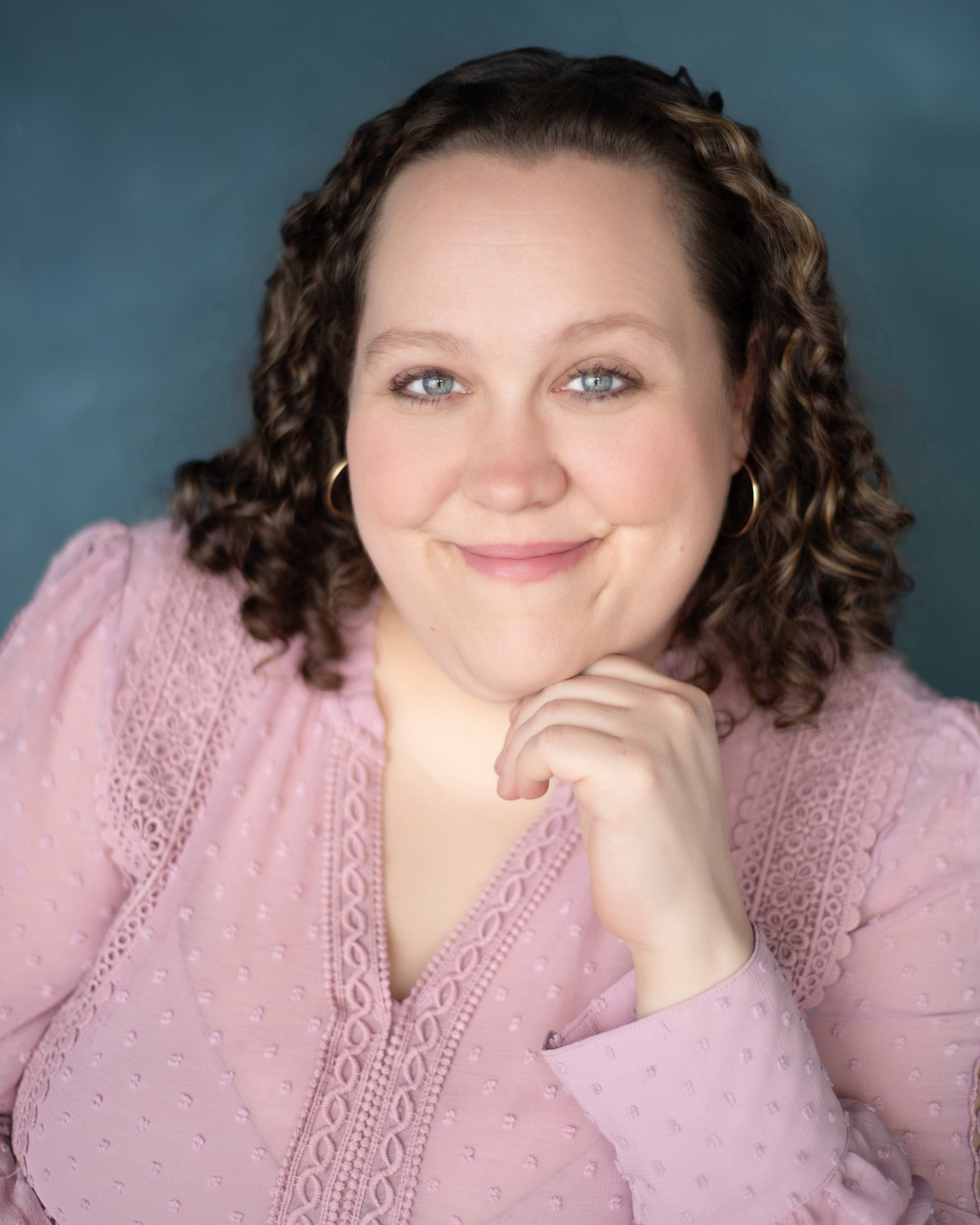 Headshot of a woman in a pink blouse in front of a blue backdrop
