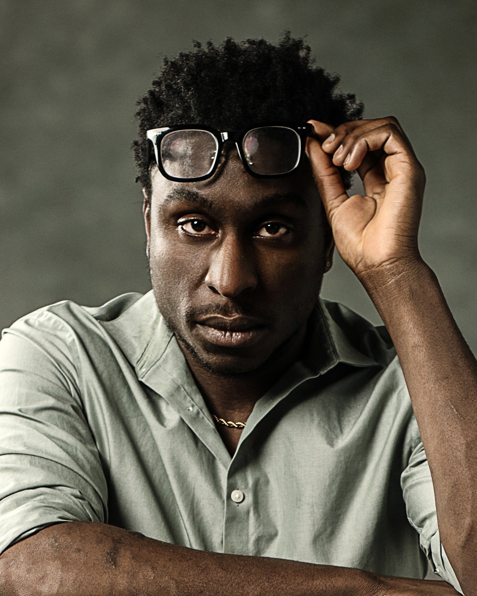 Headshot of black man holding glasses above his eyes