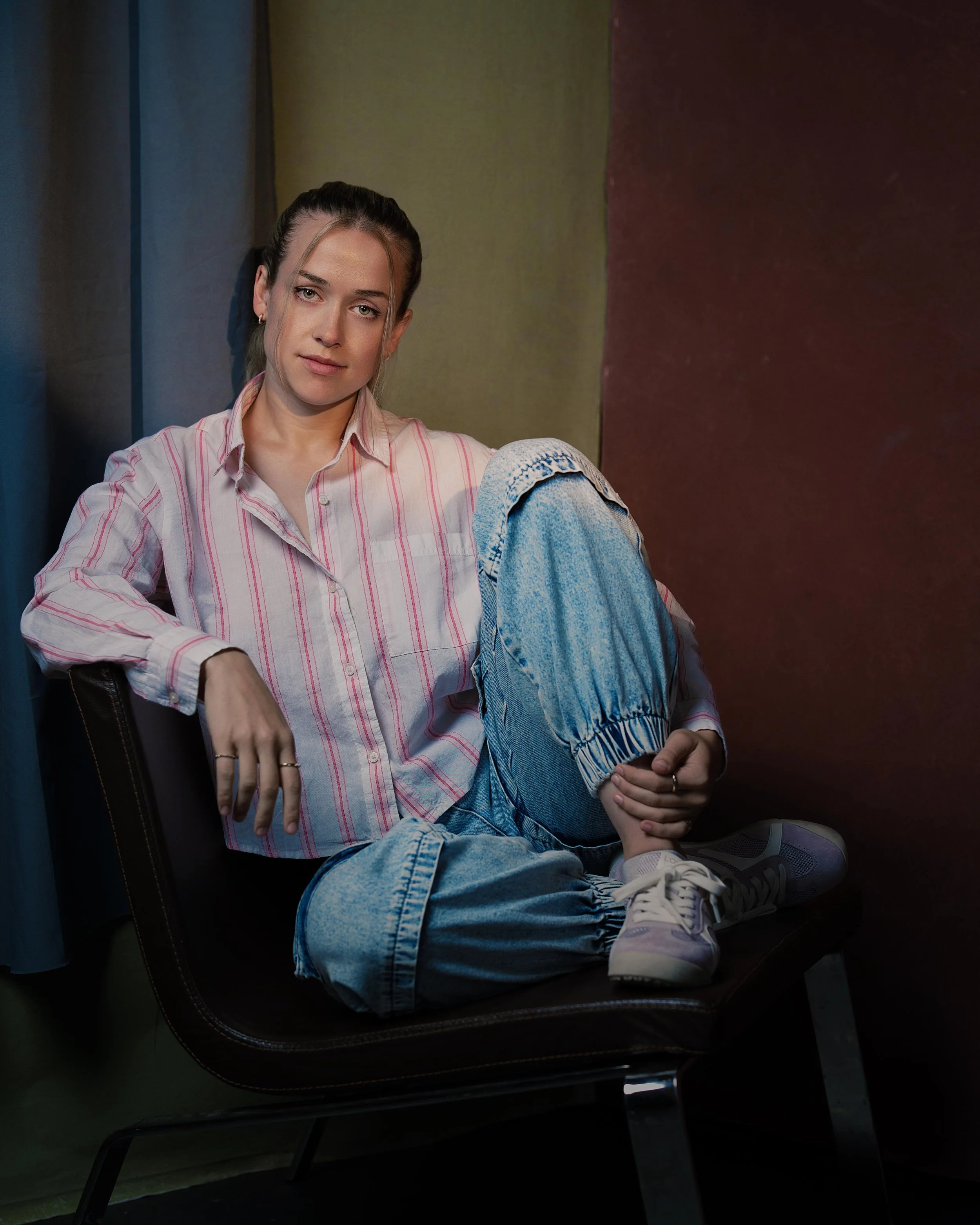 Portrait headshot of female actor sitting in brown leather vintage chair