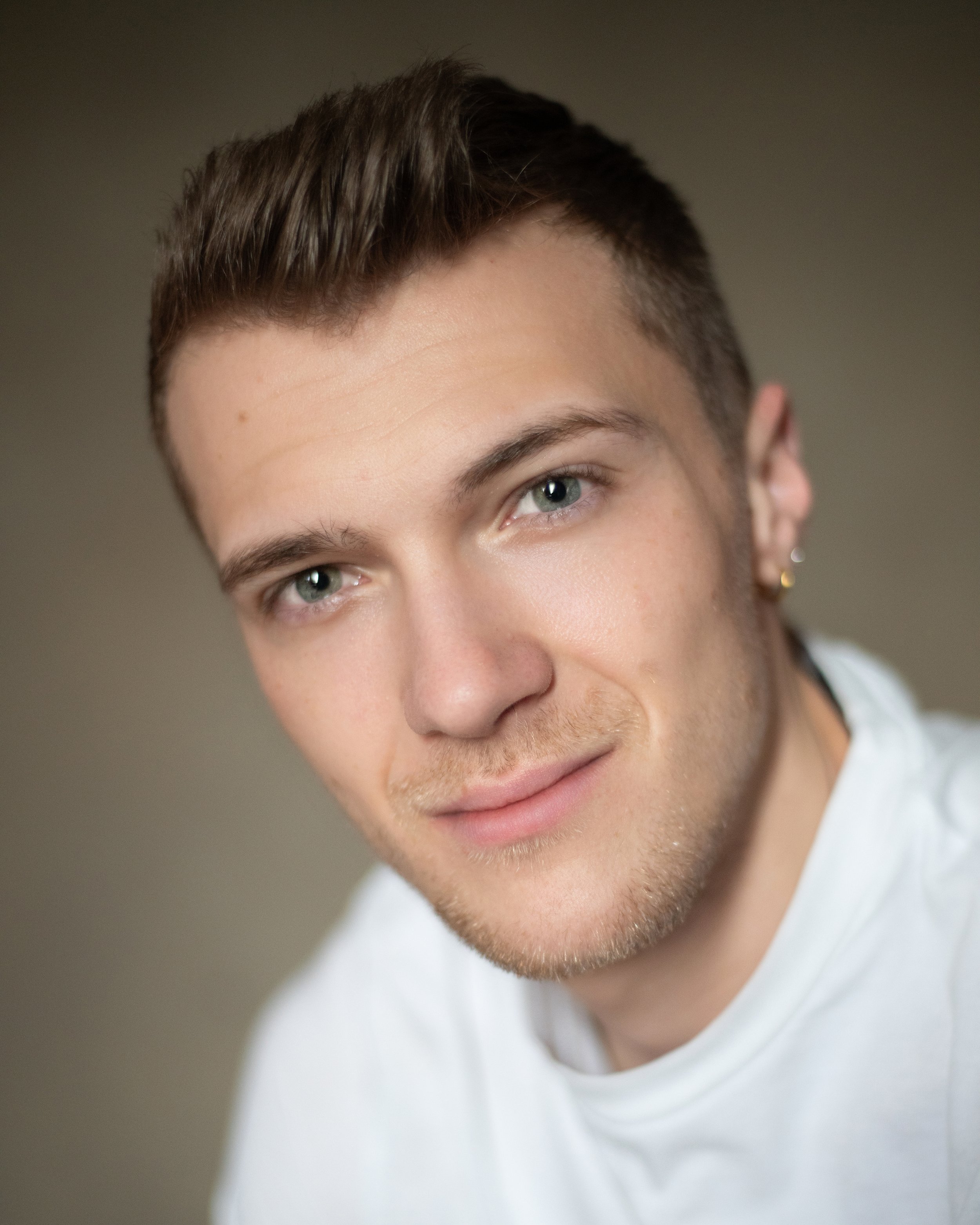 Headshot of a man in a white t-shirt in front of an olive green backdrop