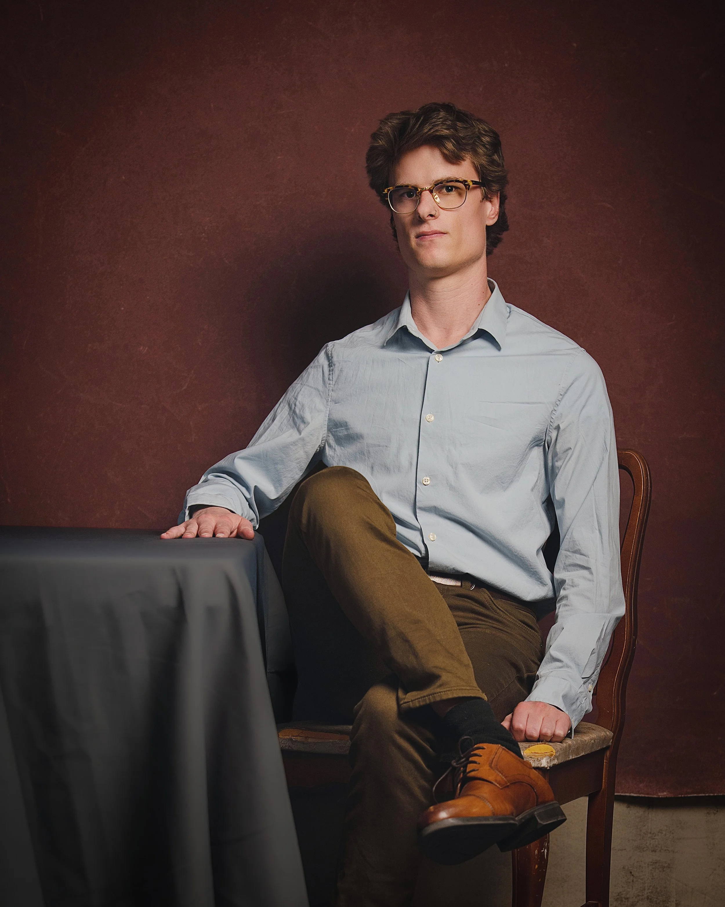 Portrait of nerdy man sitting at table with red backdrop