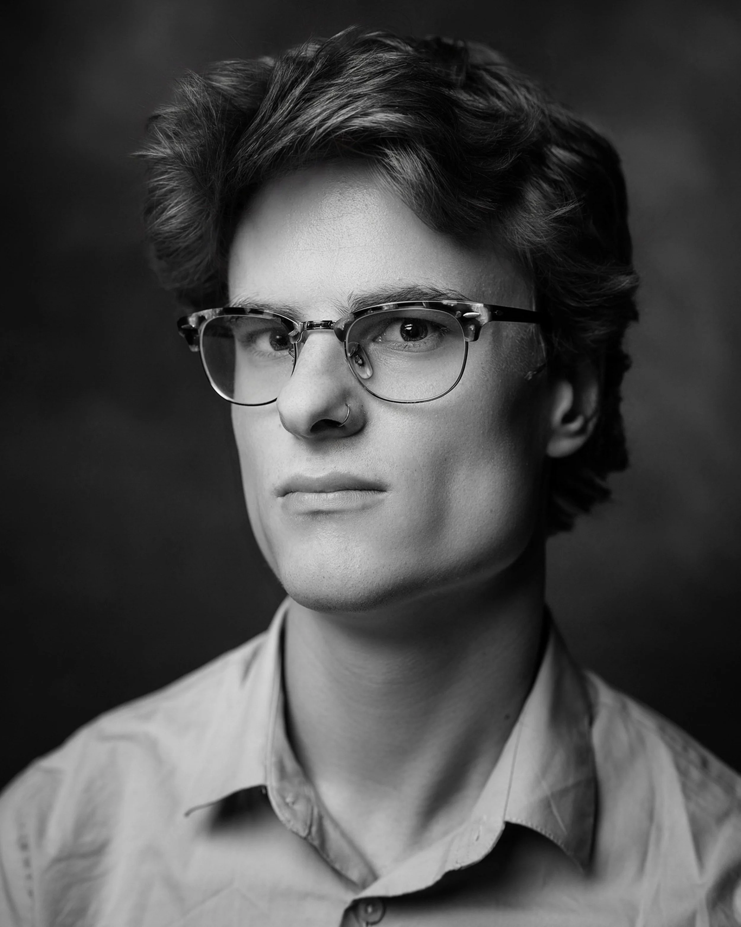 Black and white portrait of a person with short, wavy hair, wearing glasses, and a collared shirt.