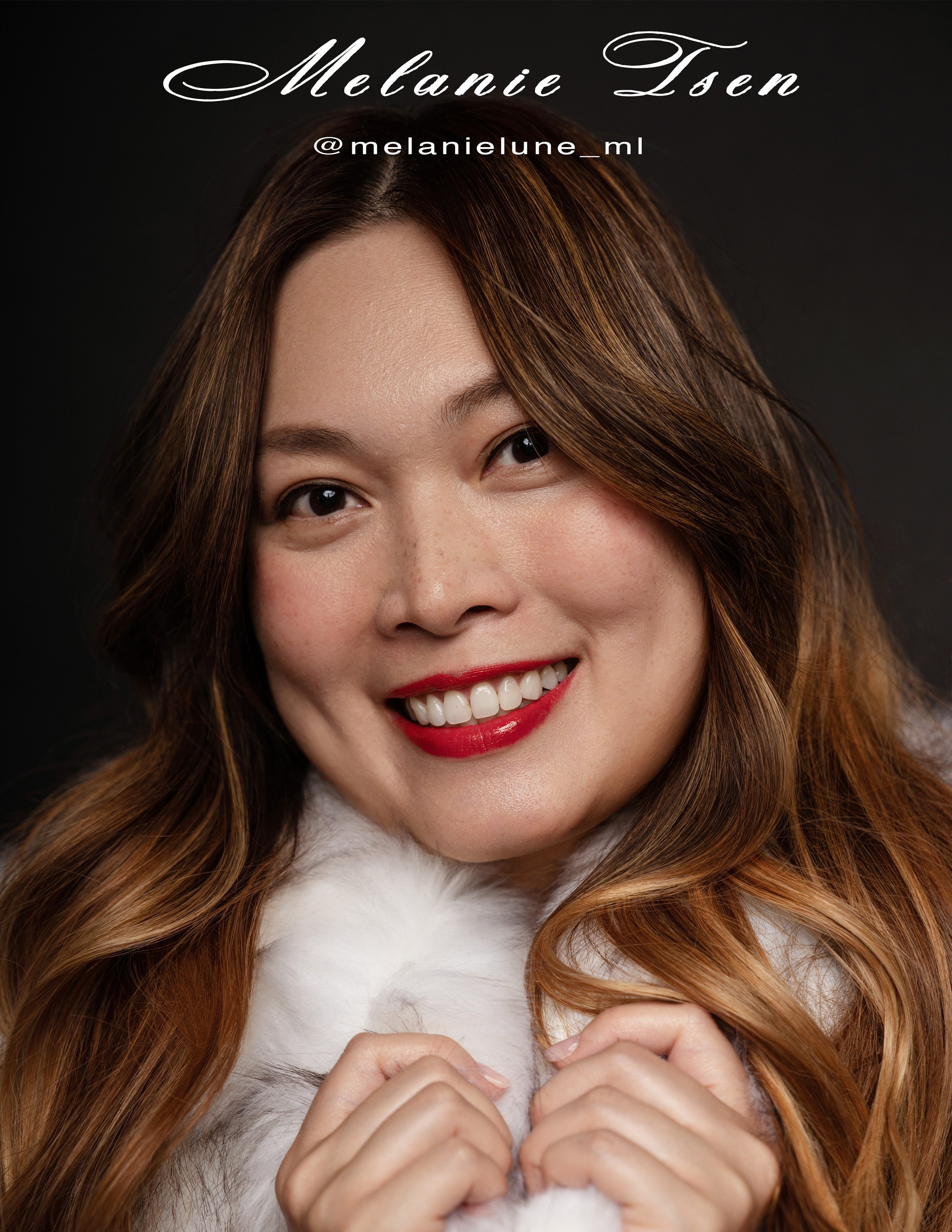 Close-up portrait of a young woman with long, wavy, reddish-brown hair, smiling, wearing red lipstick, and holding a fluffy white garment around her neck, against a black background.