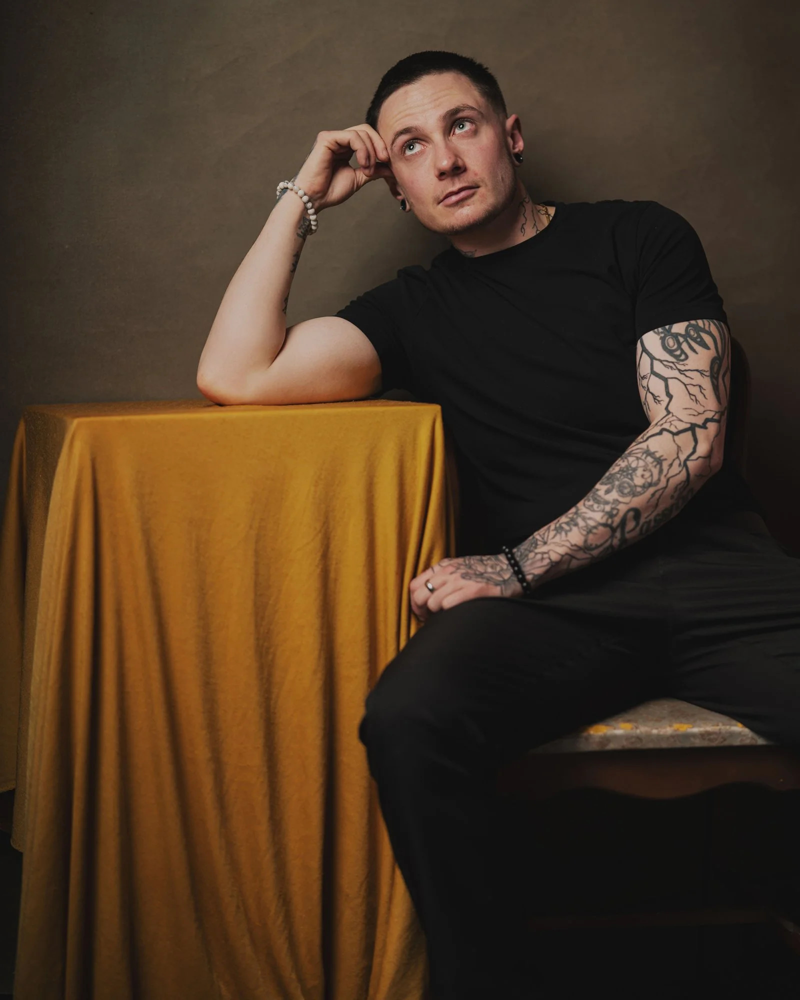 Portrait of trans man at yellow table olive green backdrob