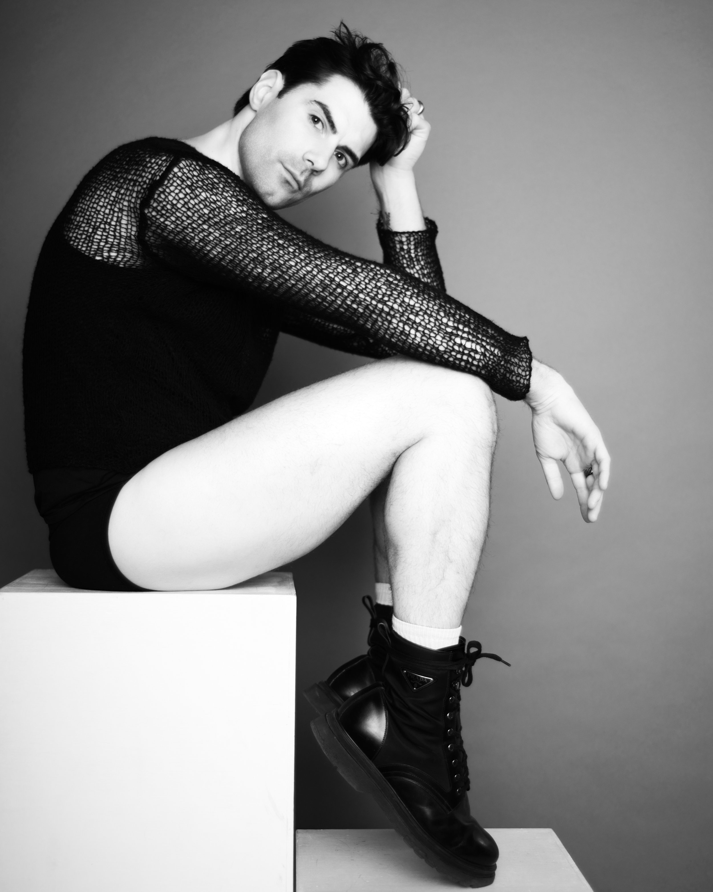 Editorial portrait of man in underwear and boots sitting on boxes