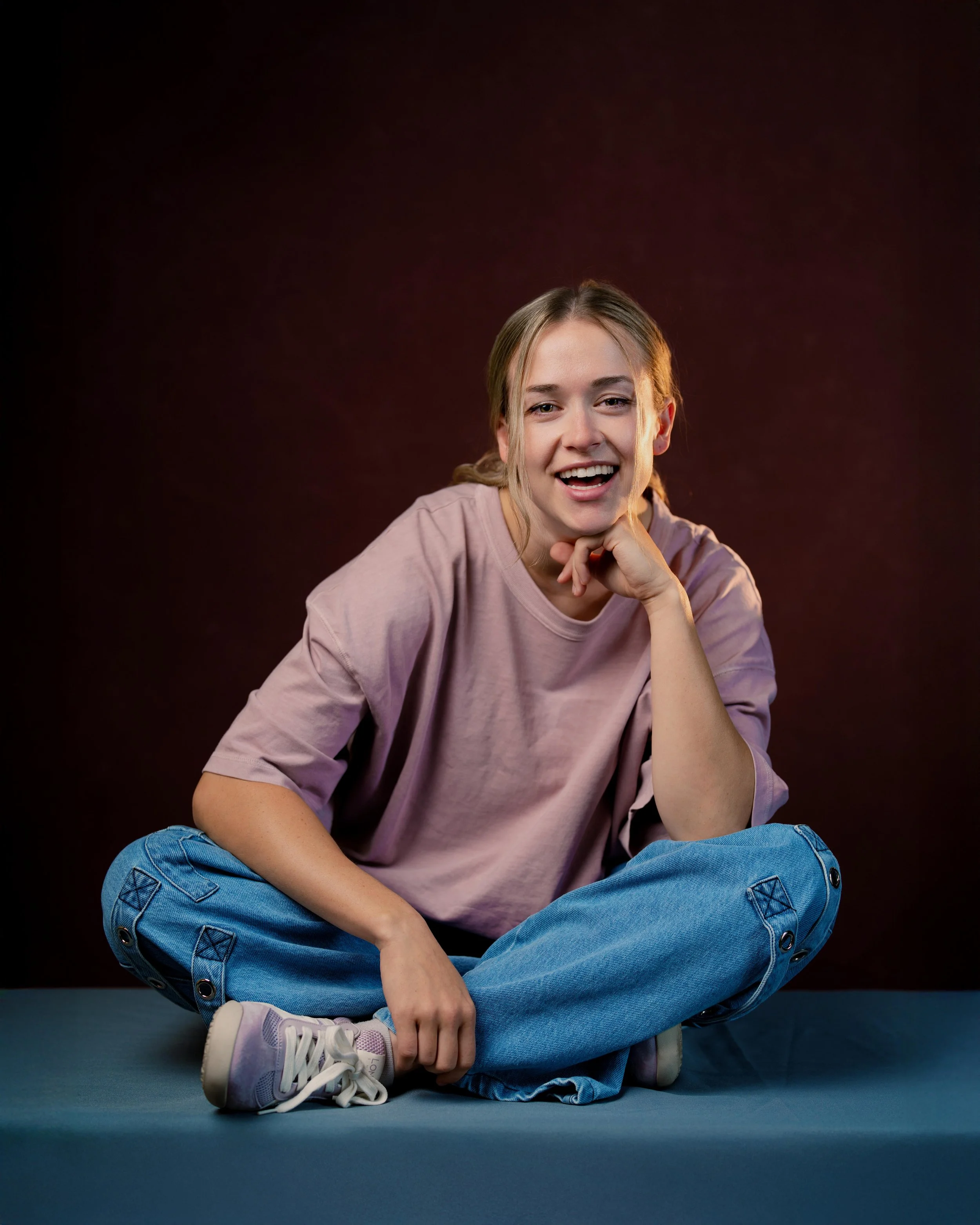 Portrait headshot of female actor sitting on blue table in pink shirt