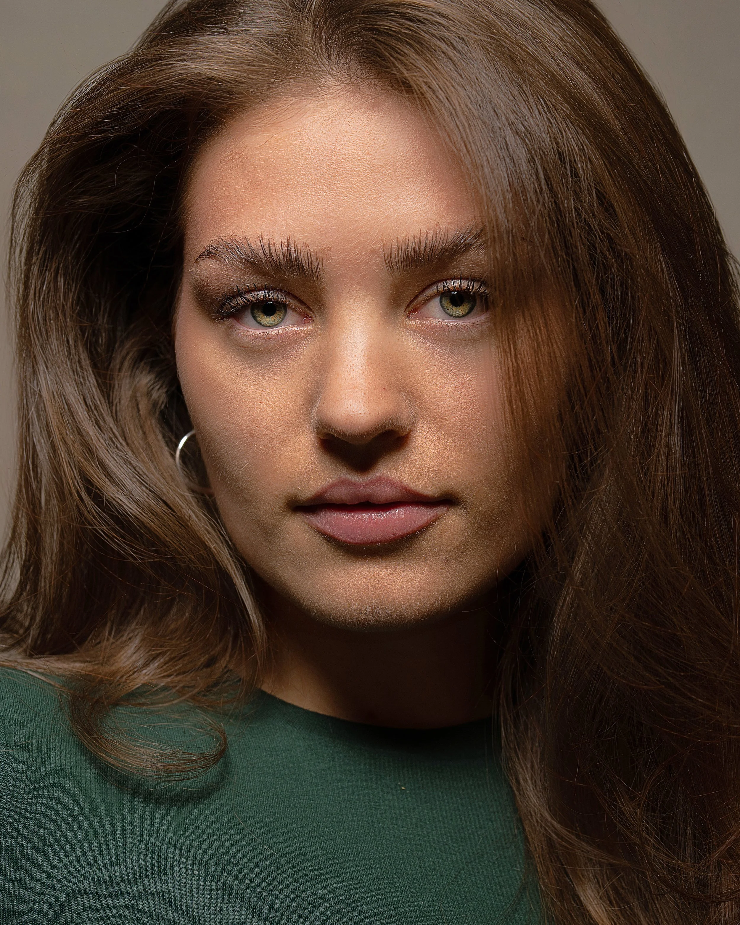 Close-up of a woman with long, wavy brown hair, green eyes, and wearing a green top.