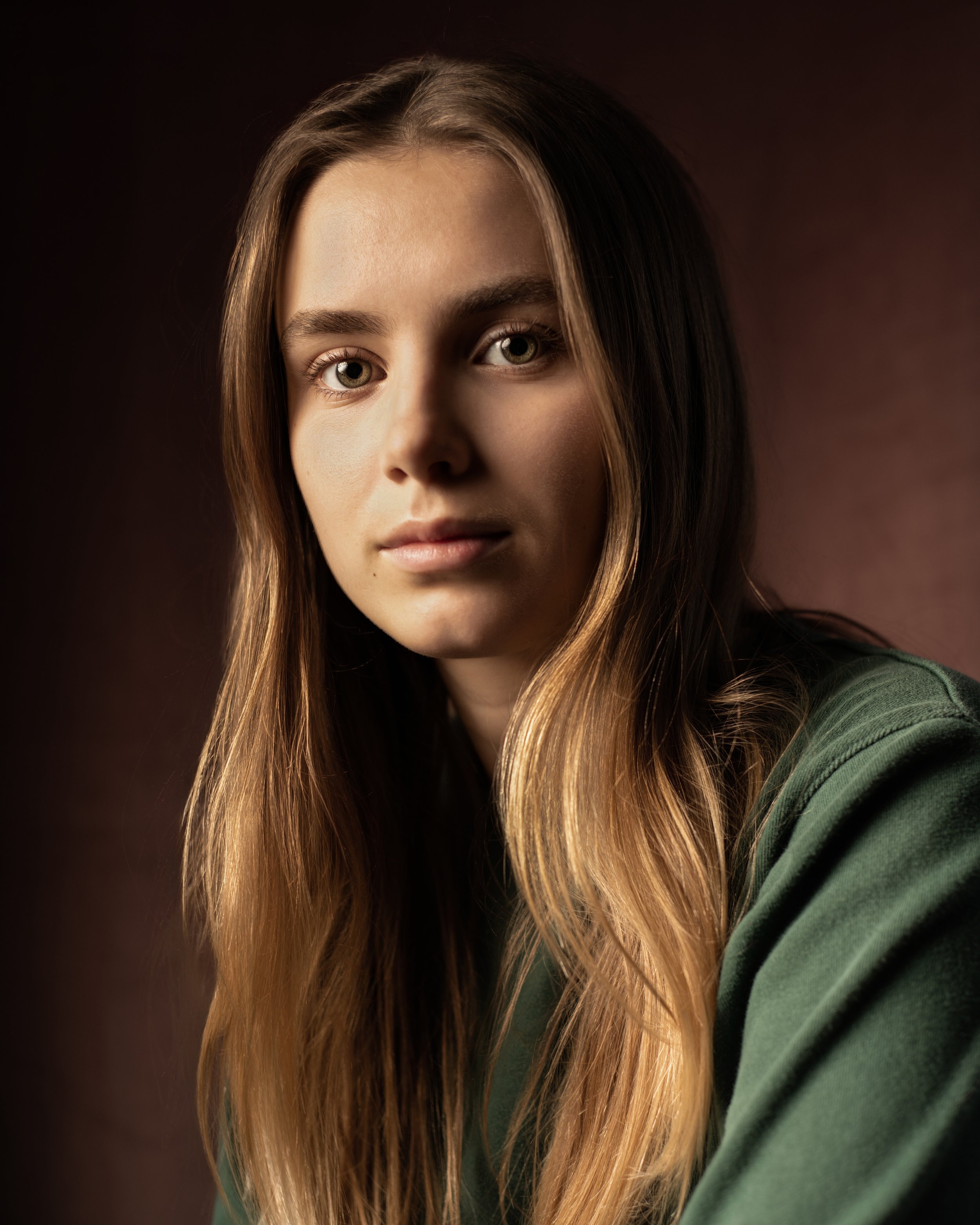 Headshot of a woman in a green sweater in front of a red backdrop
