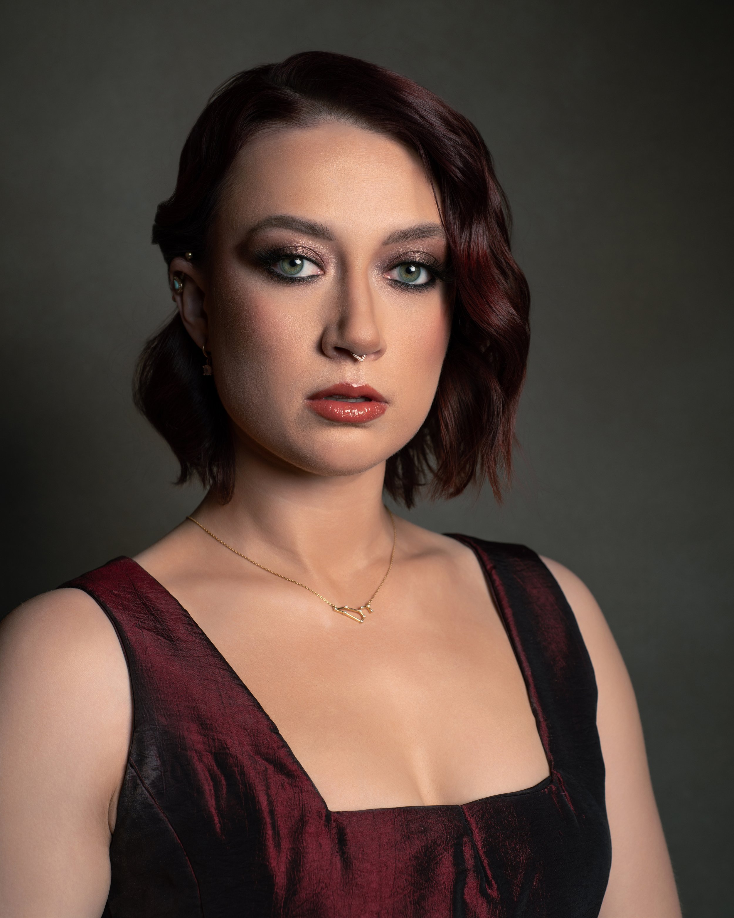 Headshot of a woman with auburn hair and shiny maroon dress in front of an olive green backdrop