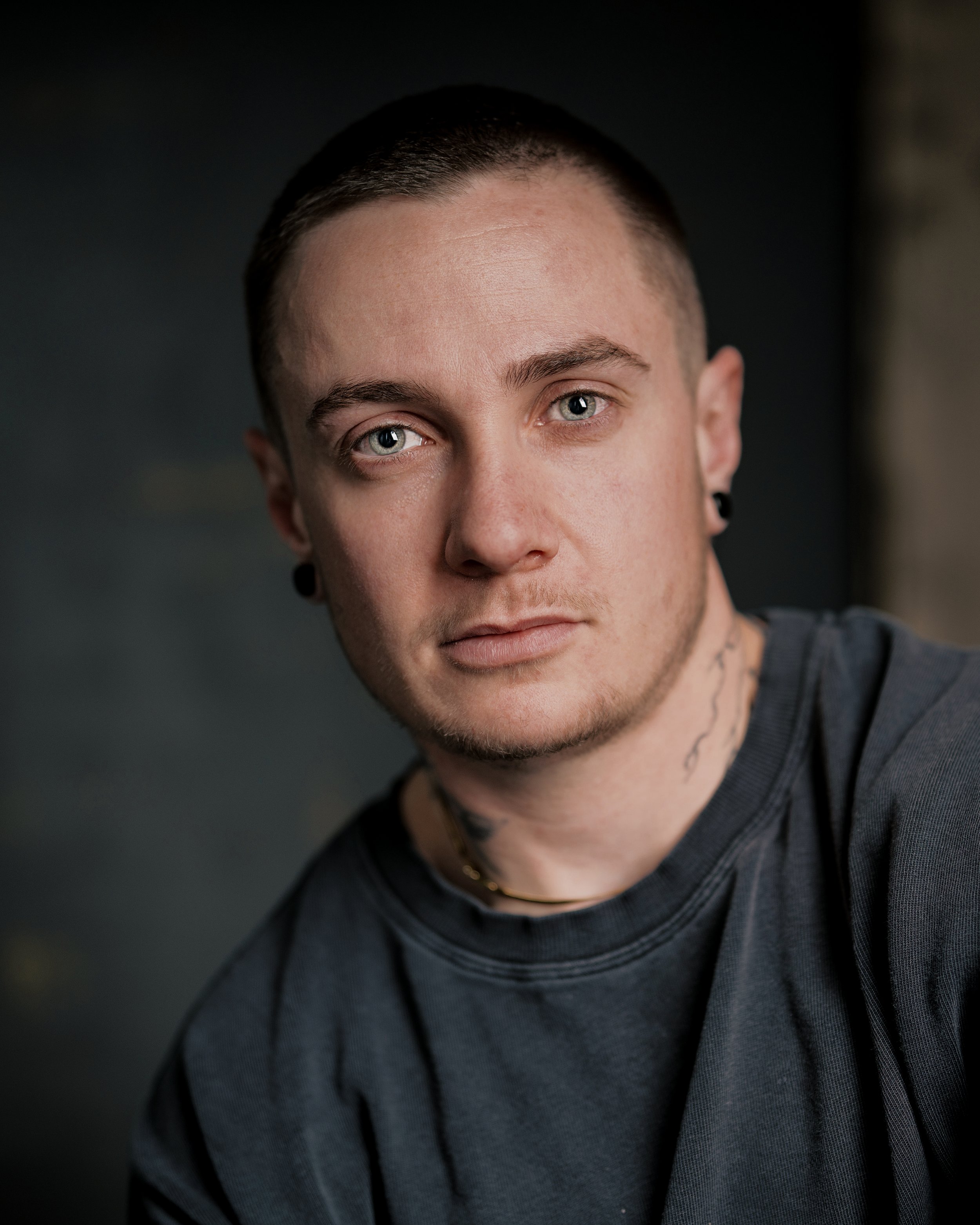 Headshot of a man with a buzz cut in a dark grey shirt in front of grey and beige backdrop