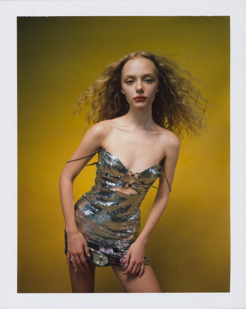 Amaiah Miller with curly hair wearing a sequined dress with cutouts against a yellow background.