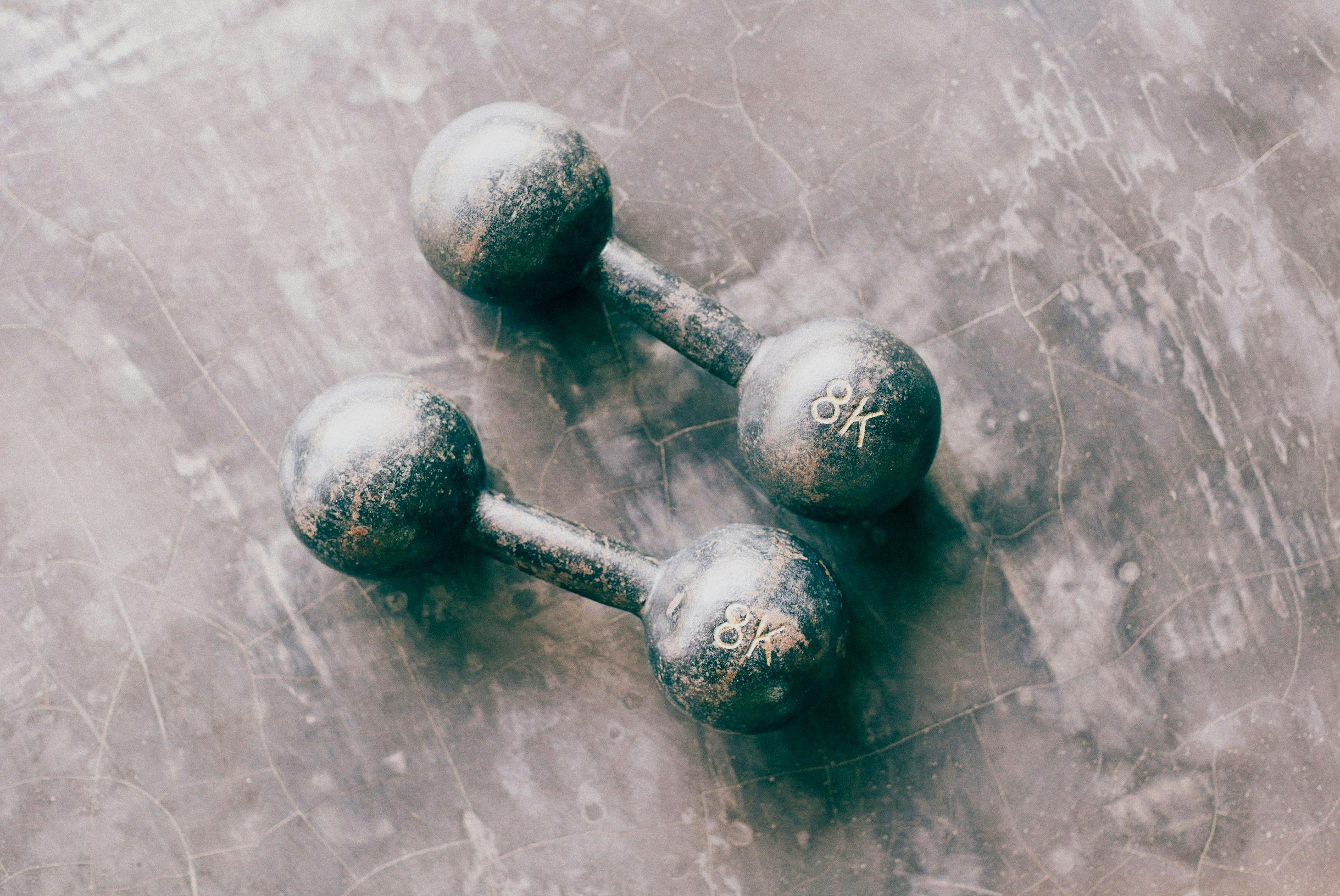 Two small, silver dumbbells with the number 8K written on each, placed on a gray, cracked surface.
