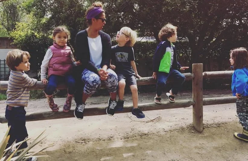 Children enjoying fun time sitting on a fence with an adult.