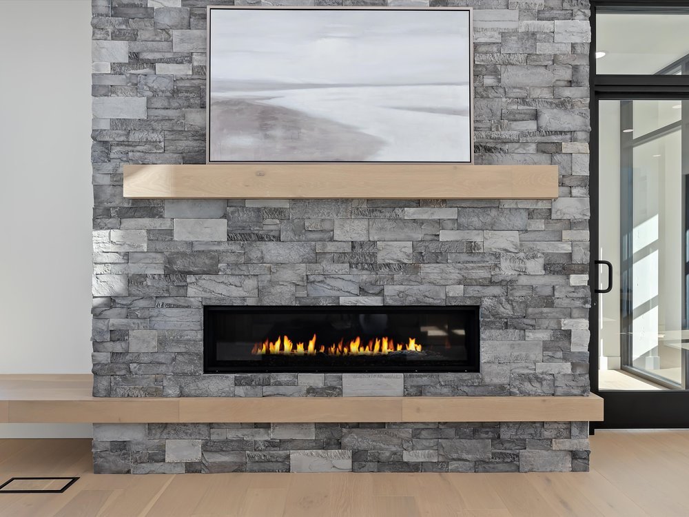Eagle, Idaho - Eco Builders Modern fireplace with gray stone surround, wooden mantel, and abstract landscape painting above.