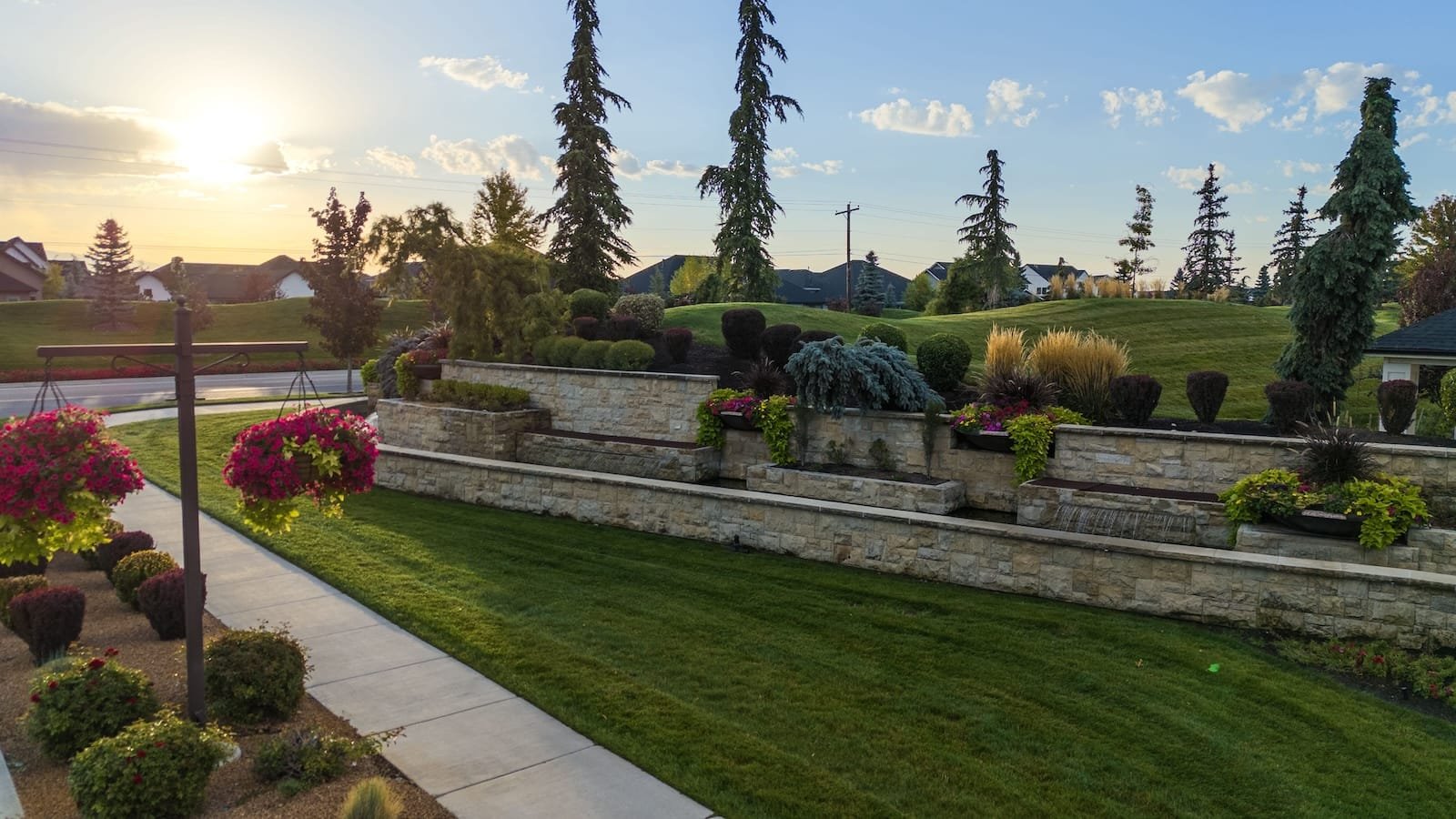 Eagle, Idaho - Landscape with stone walls, manicured bushes, hanging flower baskets, and evergreen trees at sunset.