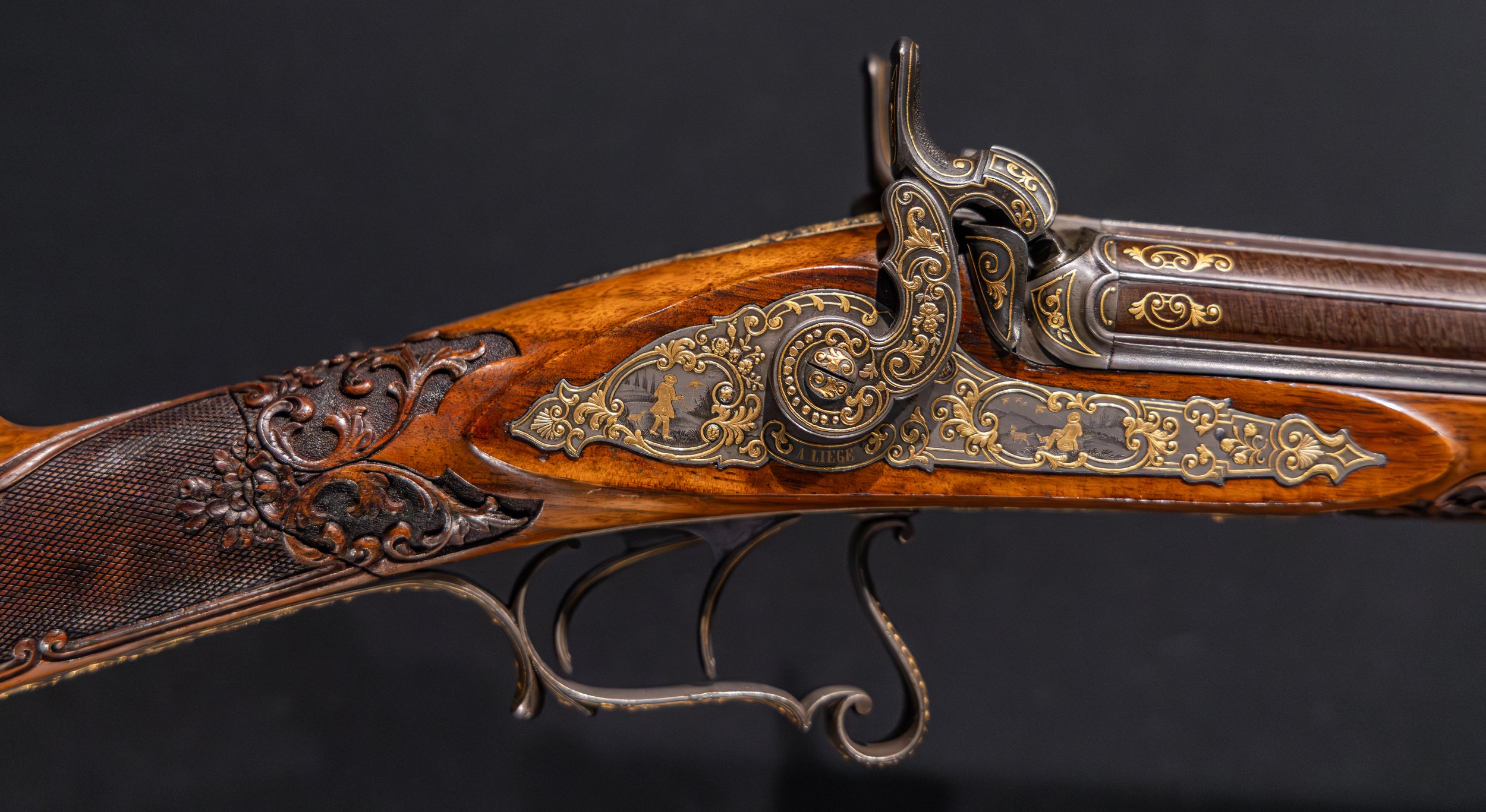 A close-up image of a highly-embellished side-by-side muzzleloading firearm with ornate wood and gold inlay.