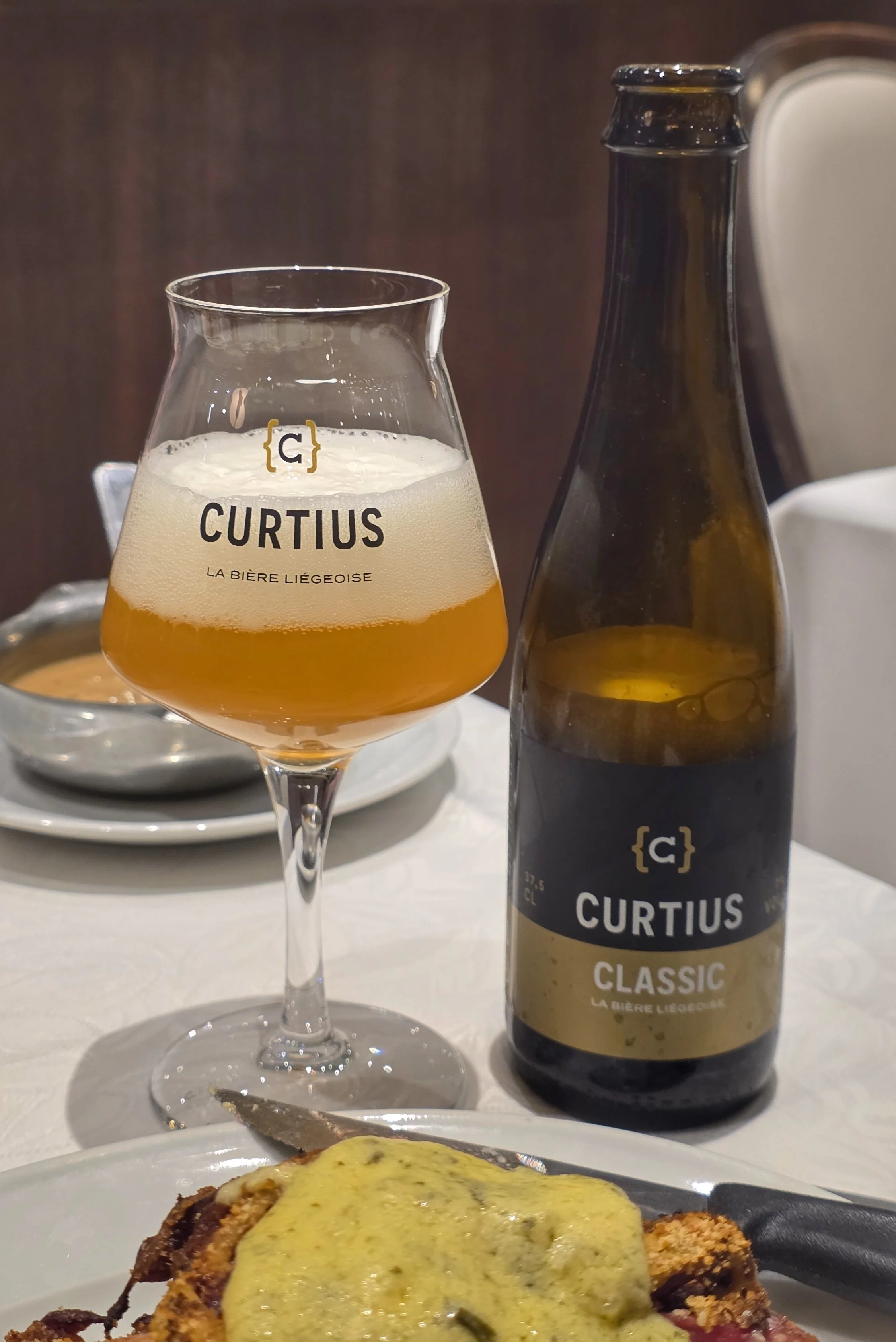 Image of a bottle of Curtius beer next to a glass carrying the Curtius logo into which the beer has recently been poured.