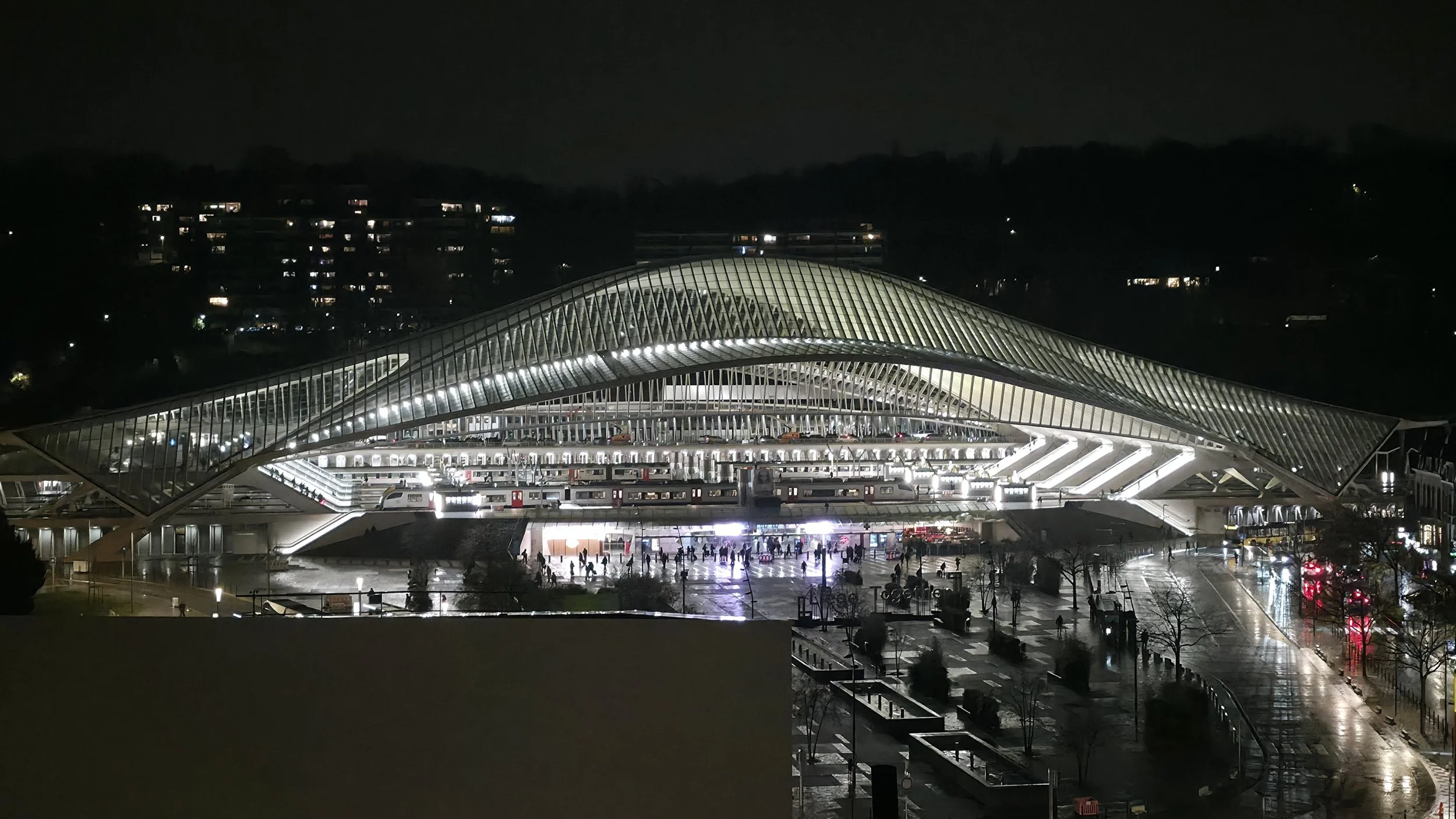 A night-time image of the train station in Liege, Belgium fully lit up and glowing in the dark, its white arching columns elegant in the stark night.
