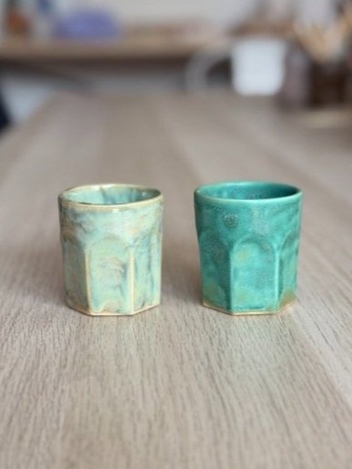 Dos tazas de cerámica de colores pastel, una en tonos verdes y otra en tonos azules, en una mesa de madera.