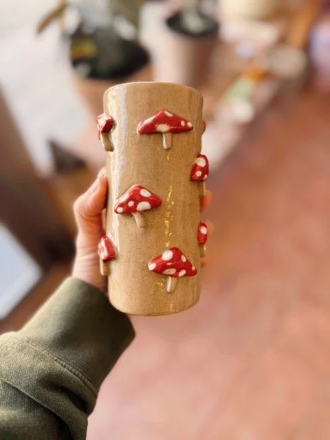 Vaso de madera decorado con mini setas rojas con puntos blancos en su superficie.