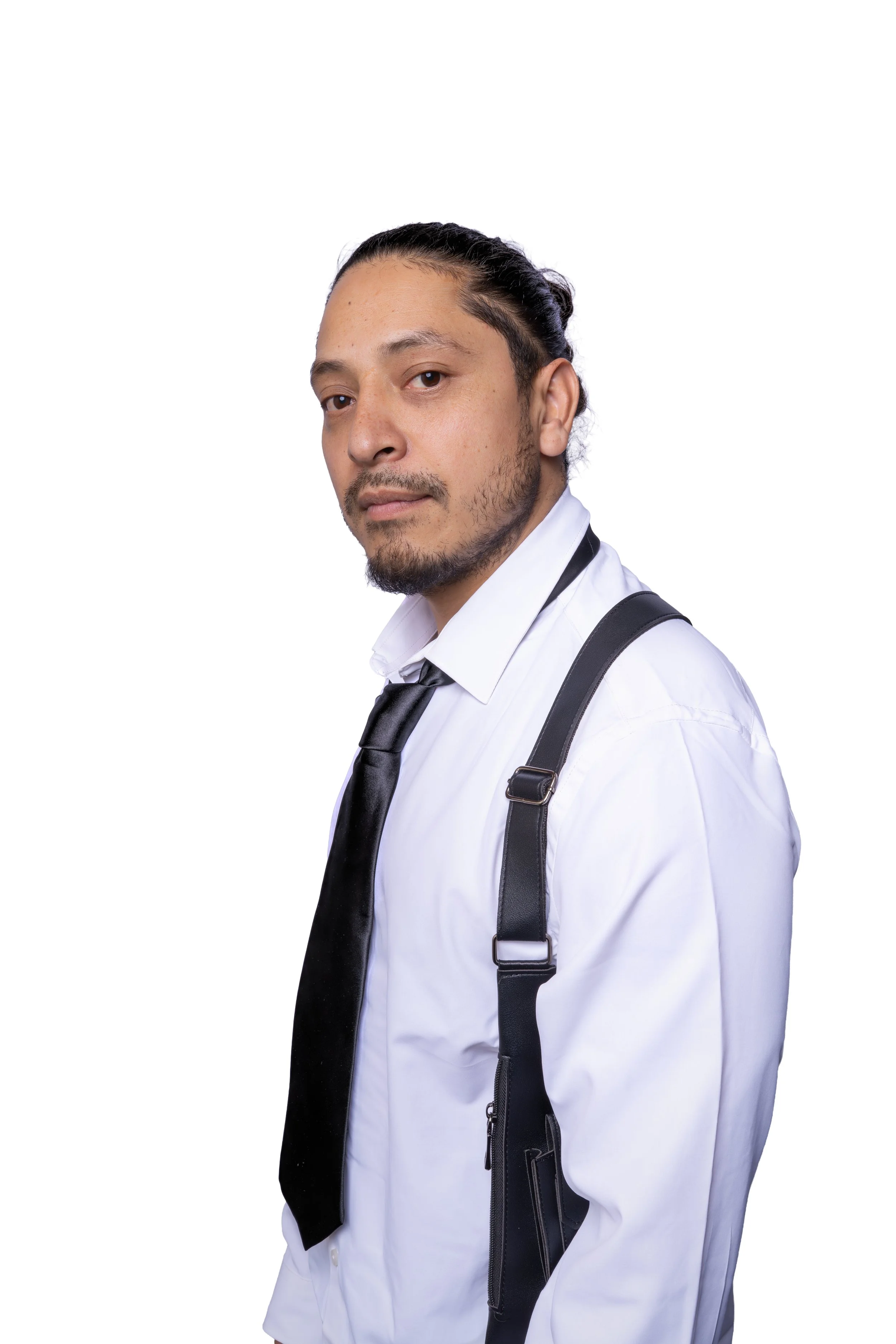 A man with dark hair, beard, and mustache wearing a white shirt, black tie, and black suspenders, looking at the camera against a plain white background.