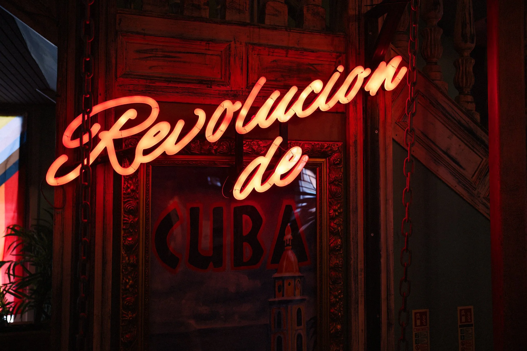 Bright red neon sign reading 'Revolution de' mounted on a dark wooden wall, with decorative woodwork framing the sign and a black chain hanging nearby.