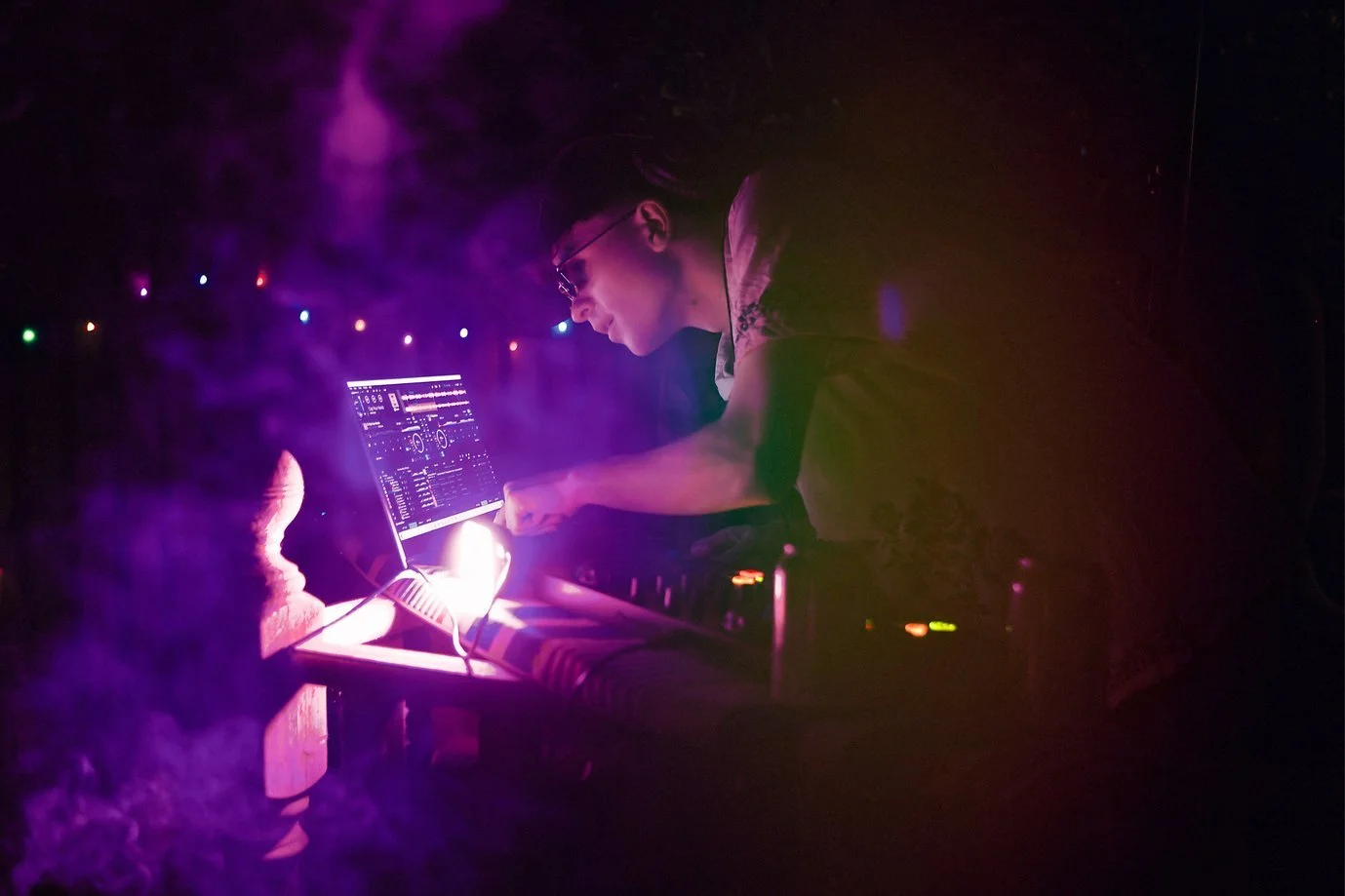 DJ performing at a nightclub with colorful lights and fog.