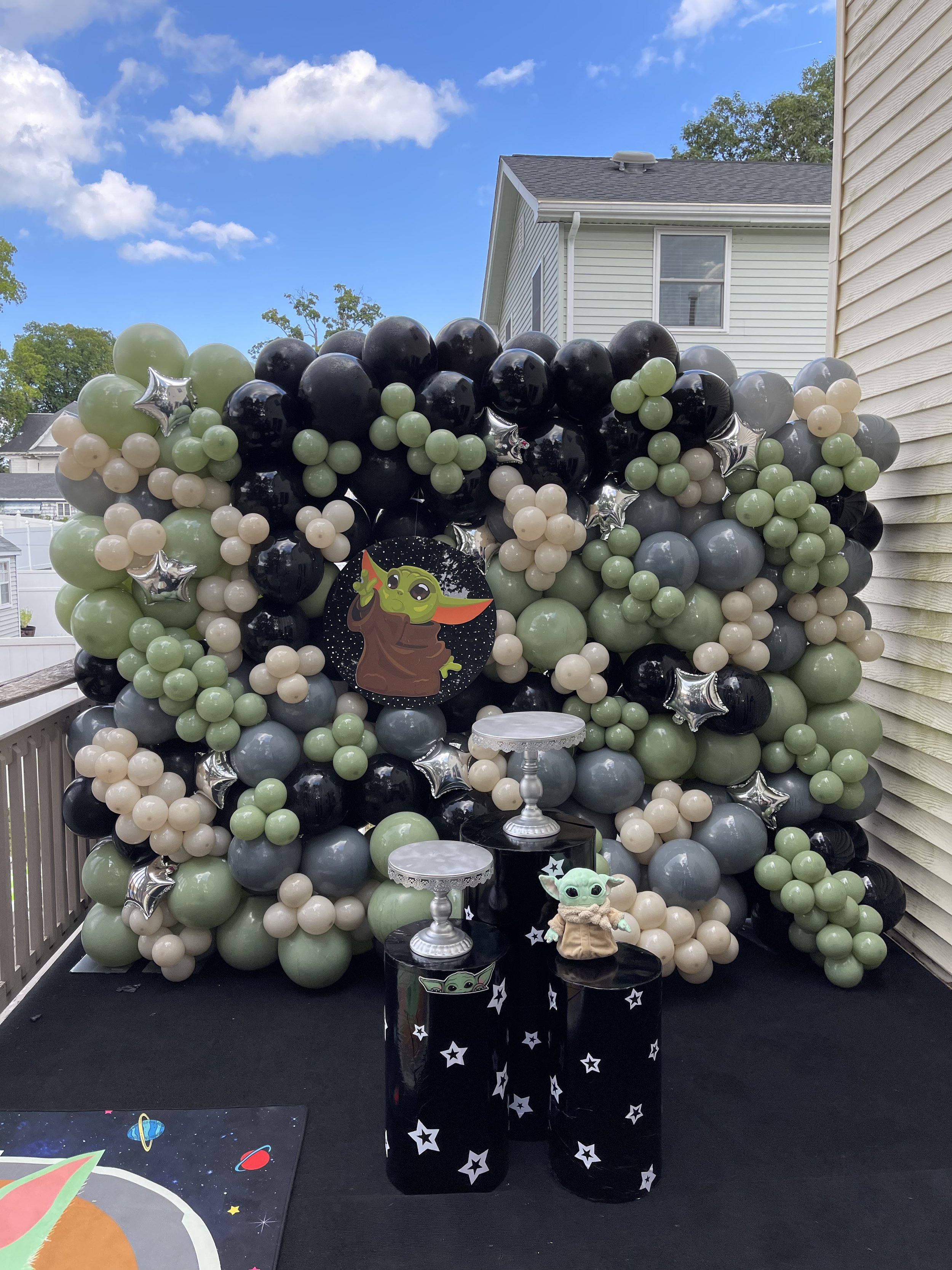 Decorative balloon backdrop featuring black, green, gray, beige, and silver balloons, with Star Wars-themed Baby Yoda (Grogu) decorations and a space-themed backdrop on the ground.