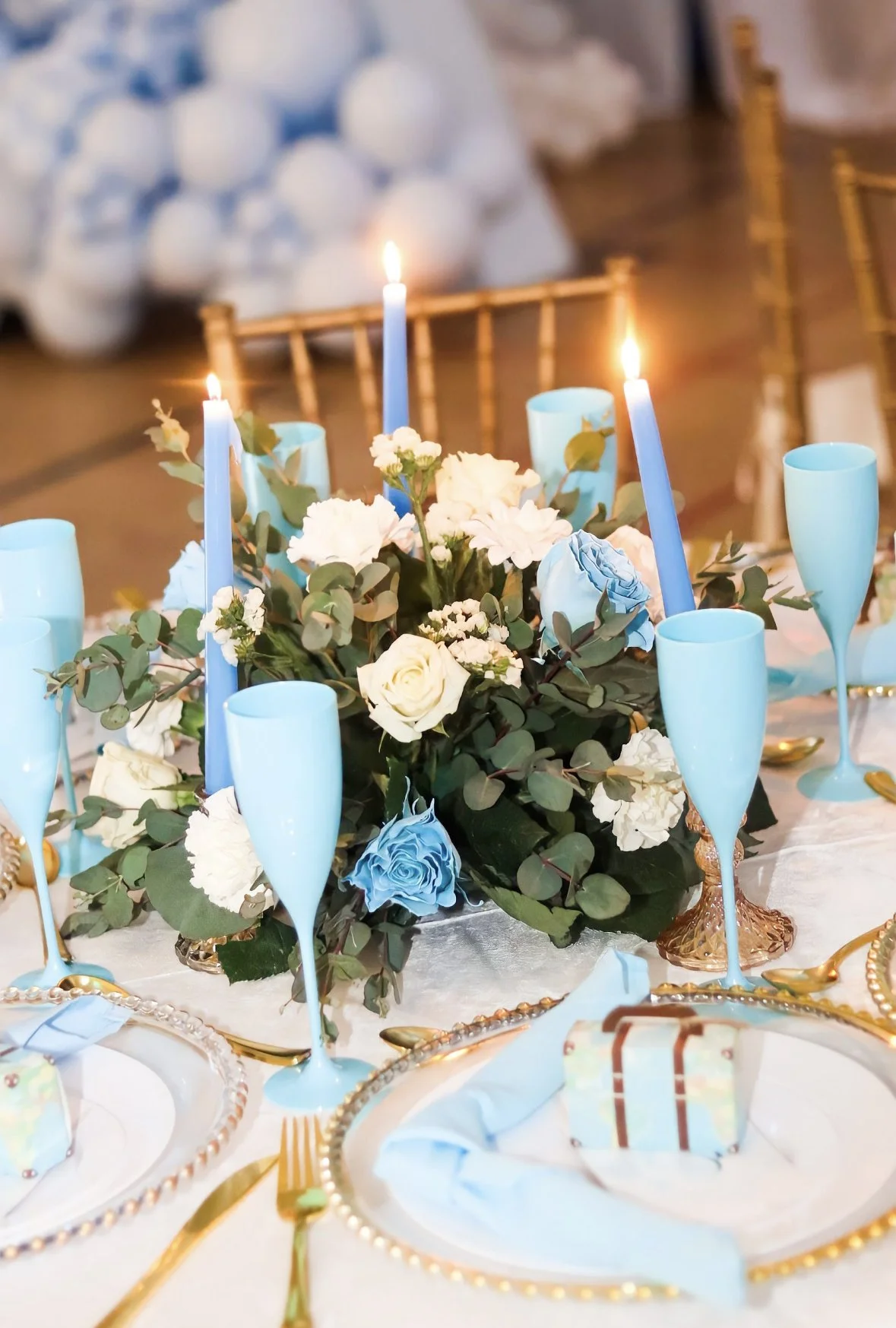 A table decorated for a celebration with a floral centerpiece, blue candles, and blue champagne glasses.