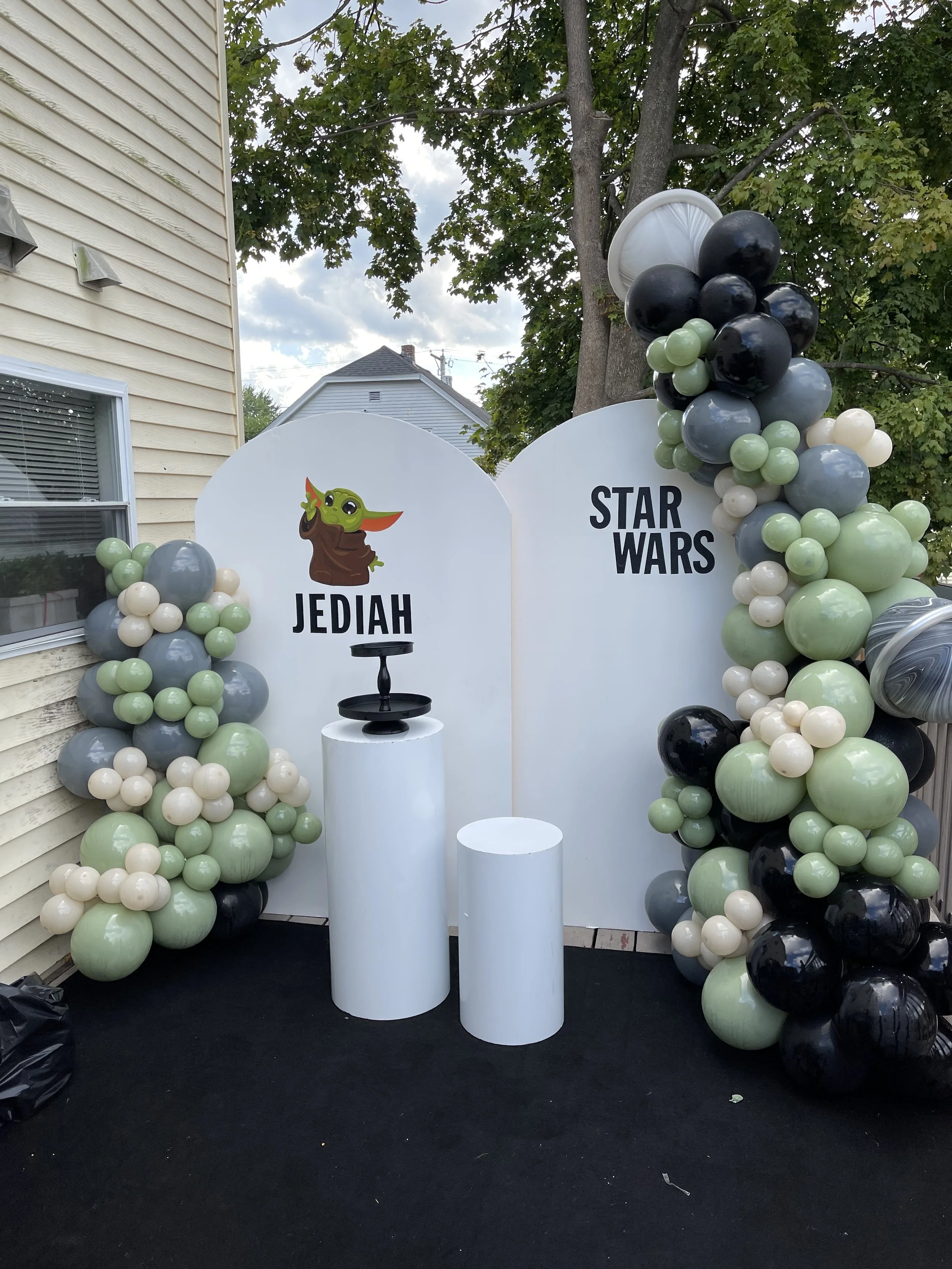 Star Wars themed photo booth with white backdrop, decorated with green, black, cream, and marble-like balloons, and a sign with a Baby Yoda graphic labeled 'Jedi' and 'Star Wars'.