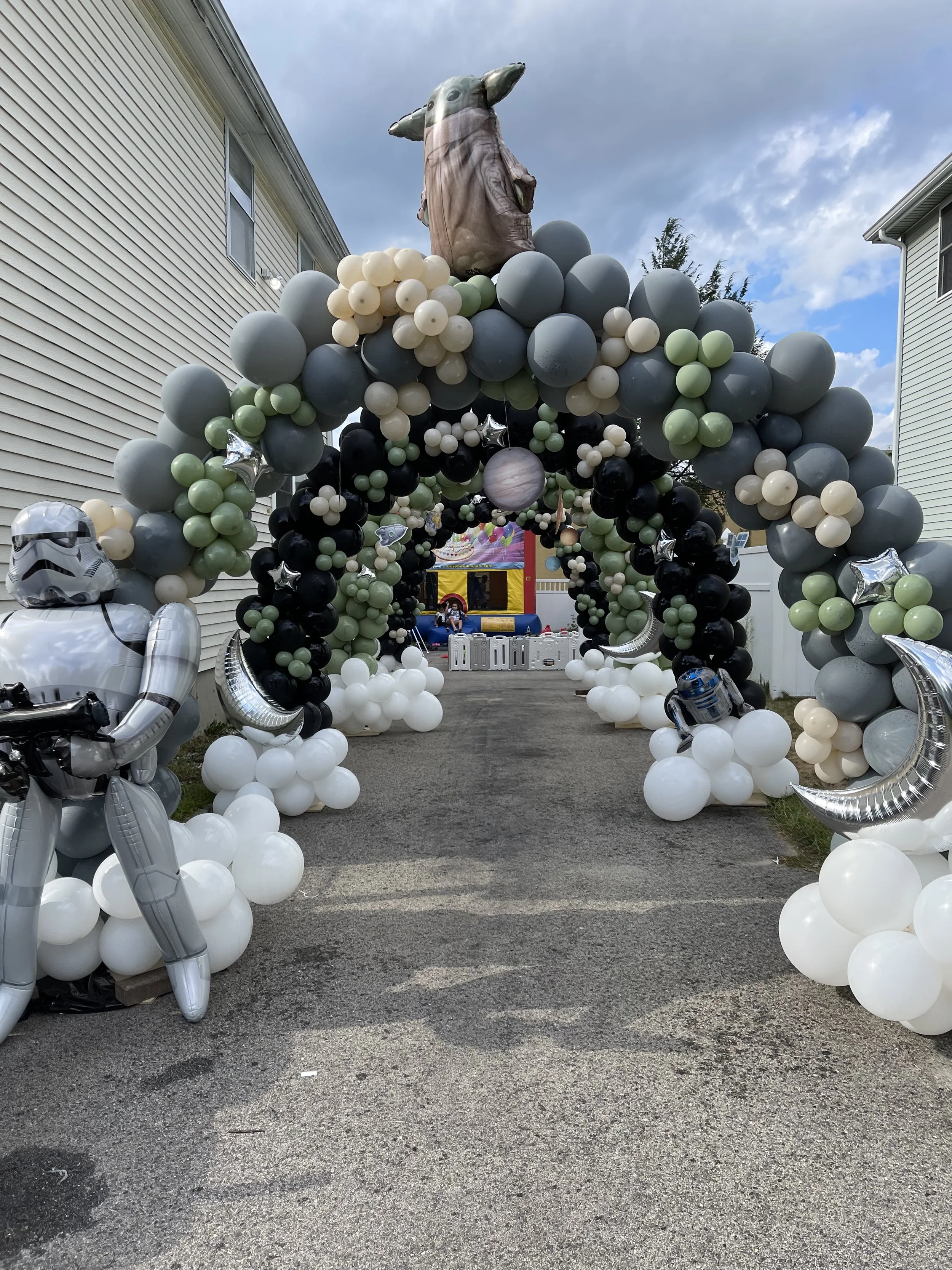 Star Wars themed balloon arch with Darth Vader, Stormtrooper, R2-D2, and Baby Yoda decorations at a birthday party.