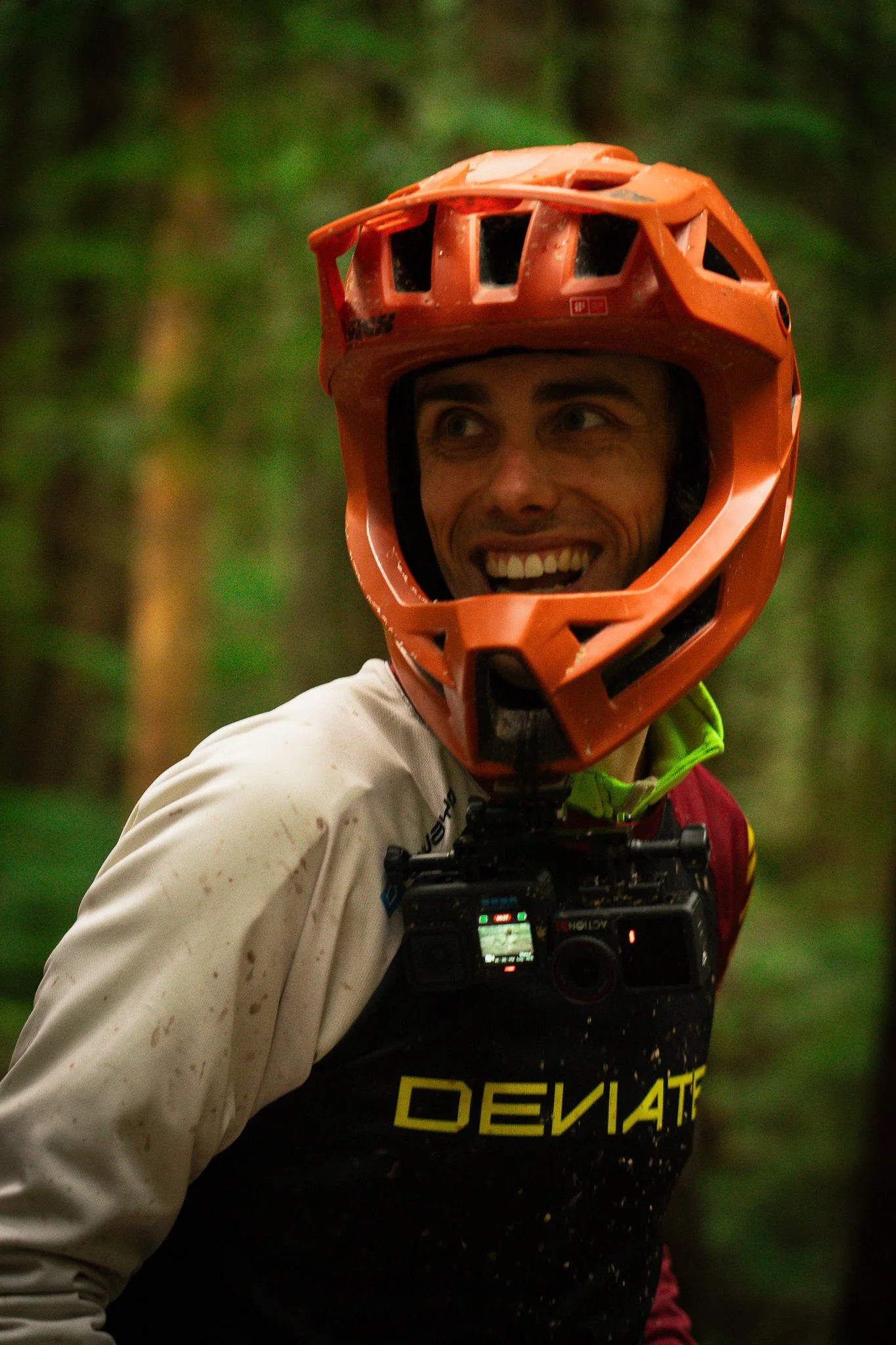 A smiling man wearing an orange mountain biking helmet, and a black bib.